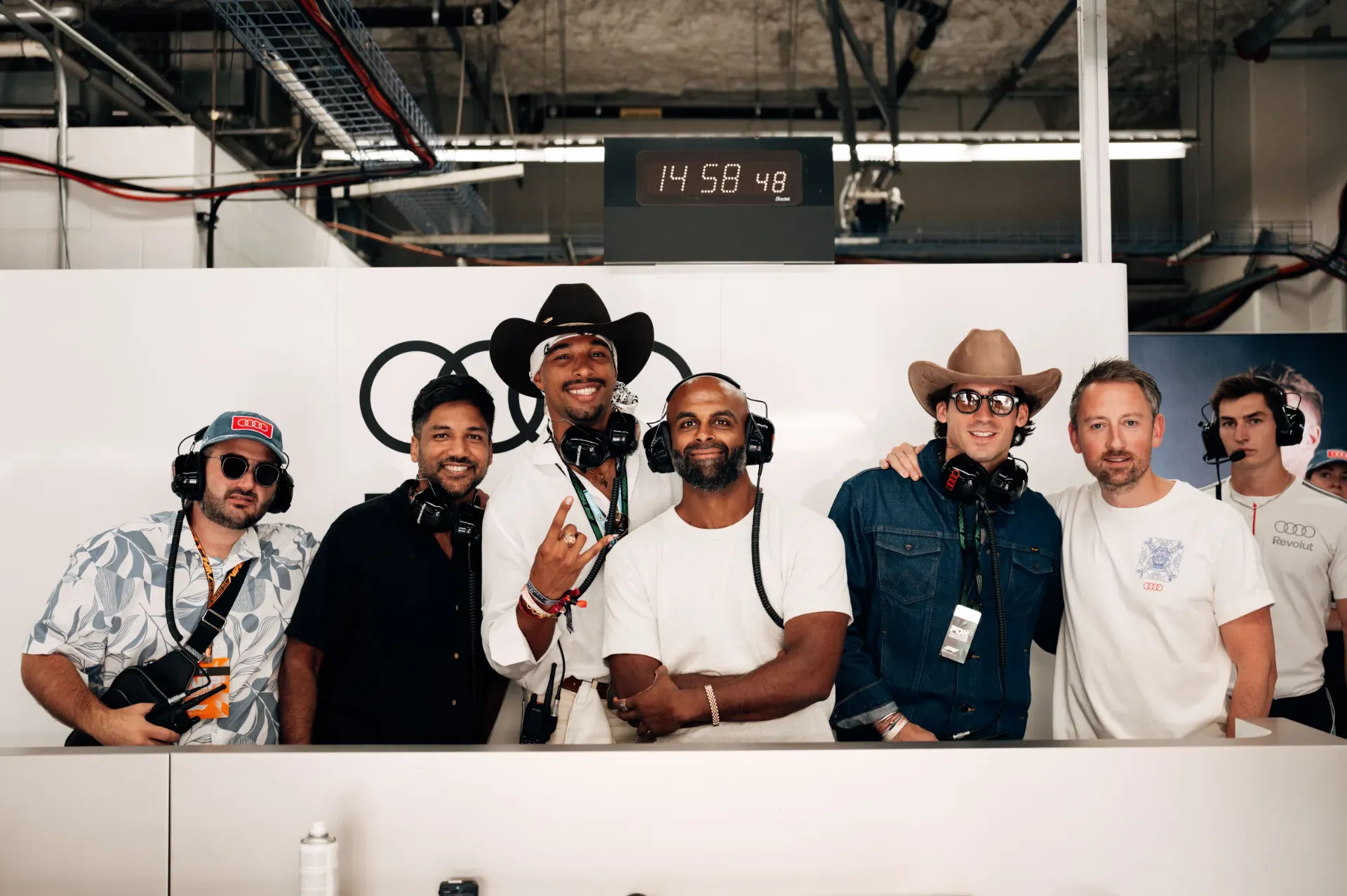 Guests wearing headsets, two in cowboy hats, posing in the Audi Revolut F1® Team garage in Austin