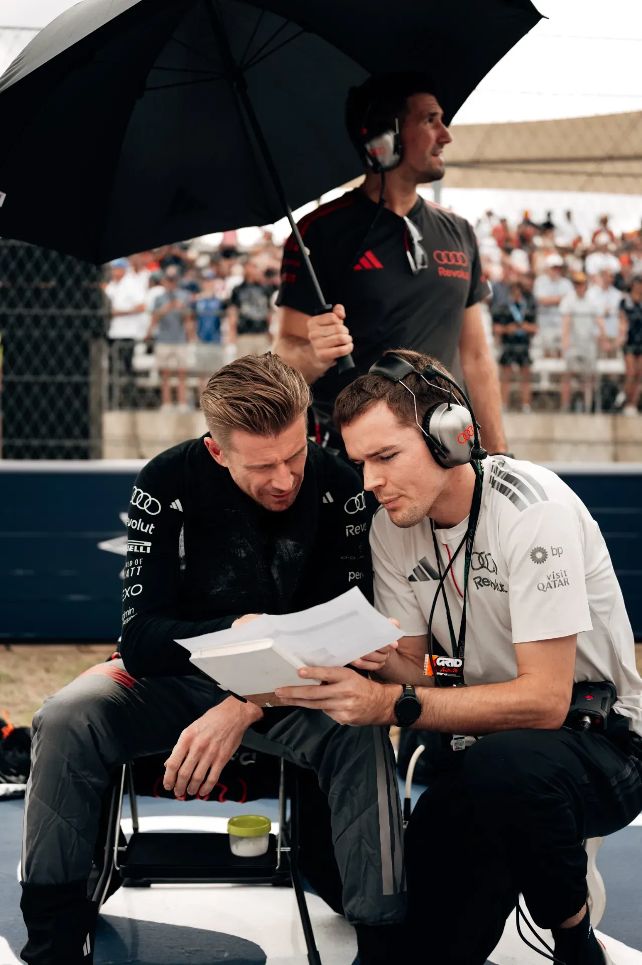 Nico Hulkenberg and an engineer of the Audi Revolut F1® Team reading papers on the grid in Austin, a mechanic with umbrella behind