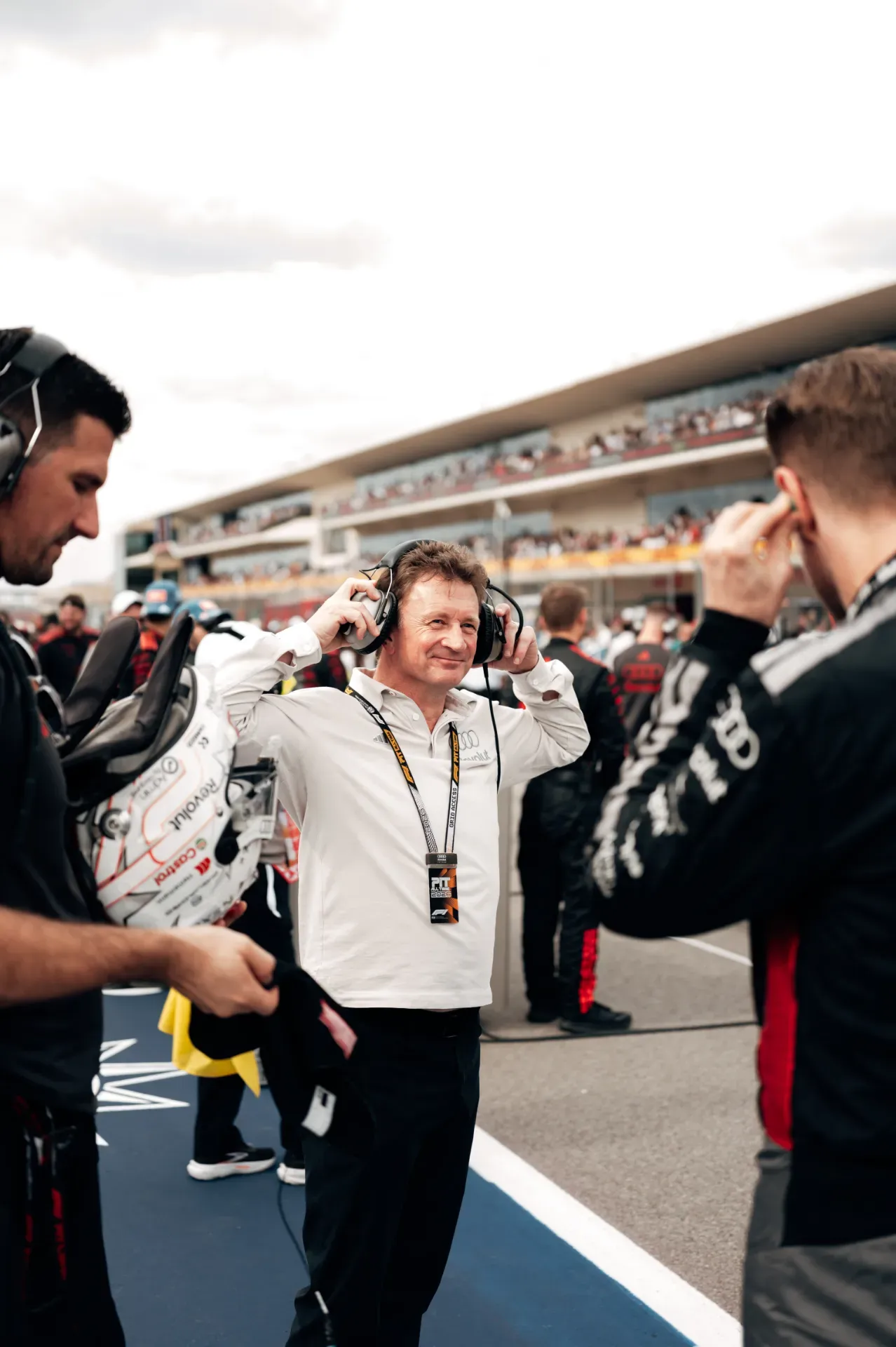 Allan McNish of the Audi Revolut F1® Team in a white shirt putting on a headset on the grid in Austin
