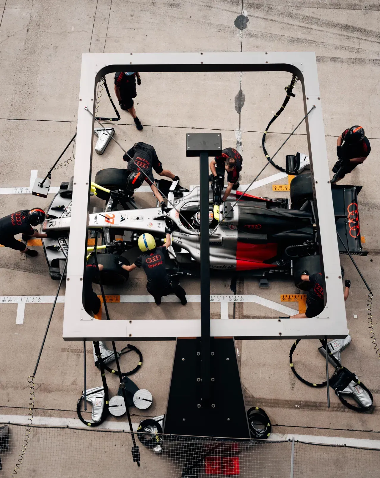 Mechanics of the Audi Revolut F1® Team change tyres on a car during a pit stop in Austin, seen from above