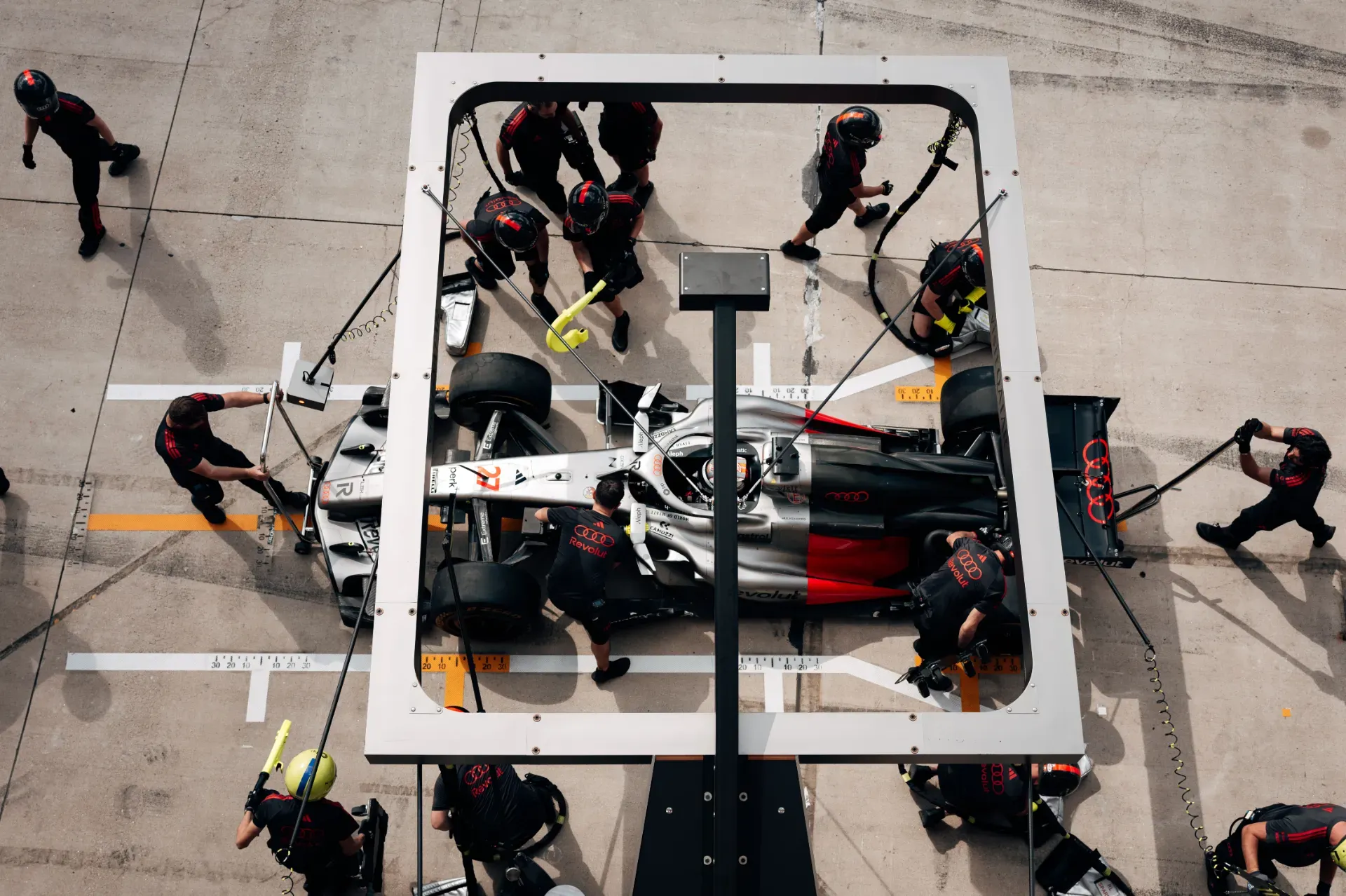 Mechanics of the Audi Revolut F1® Team service a car in a pit stop in Austin, seen from above through the overhead gantry