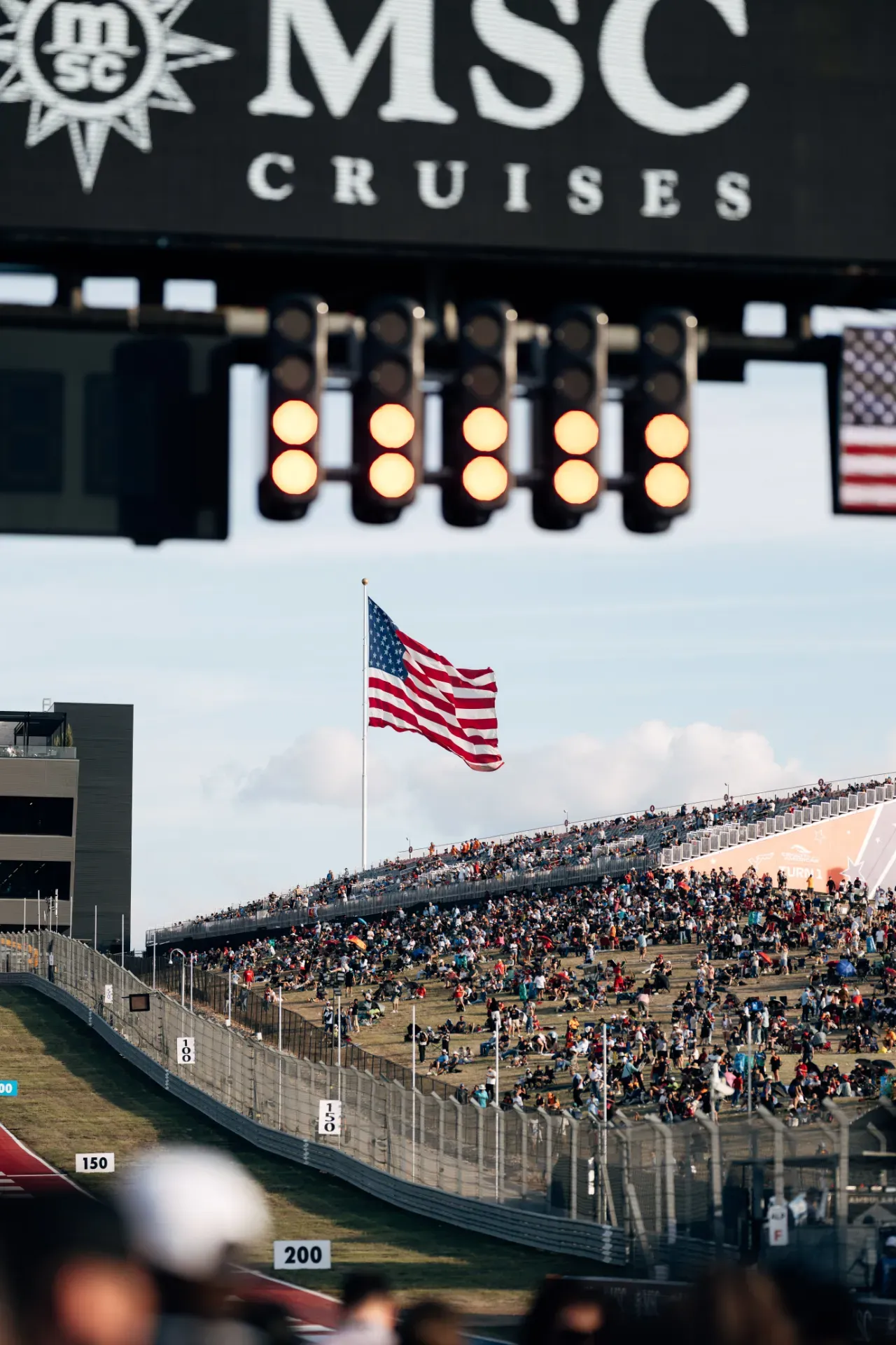 Start lights above the track with a large US flag and a crowded grandstand at the United States Grand Prix in Austin