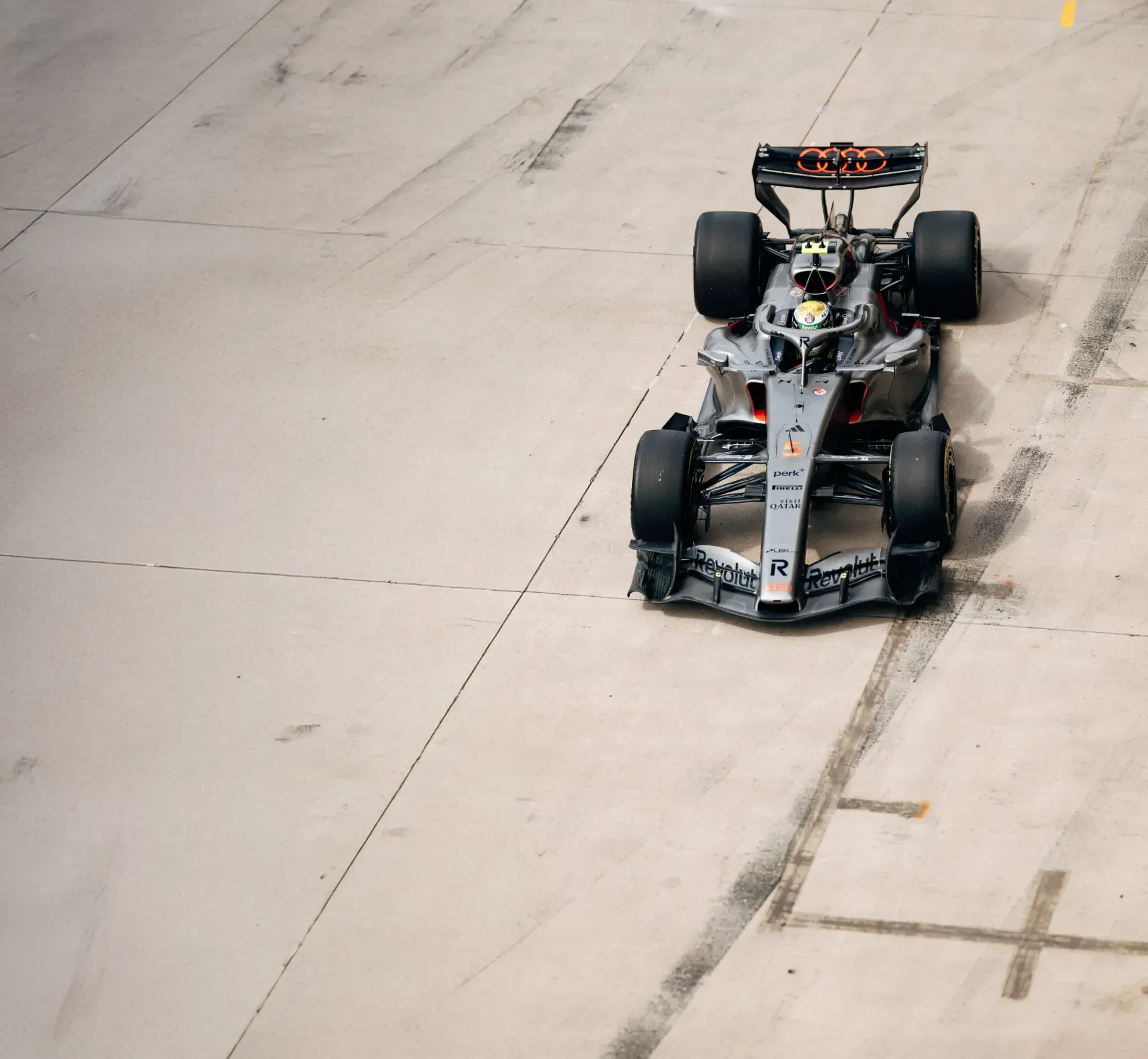 Car of the Audi Revolut F1® Team with a driver in a yellow-green helmet on a concrete surface