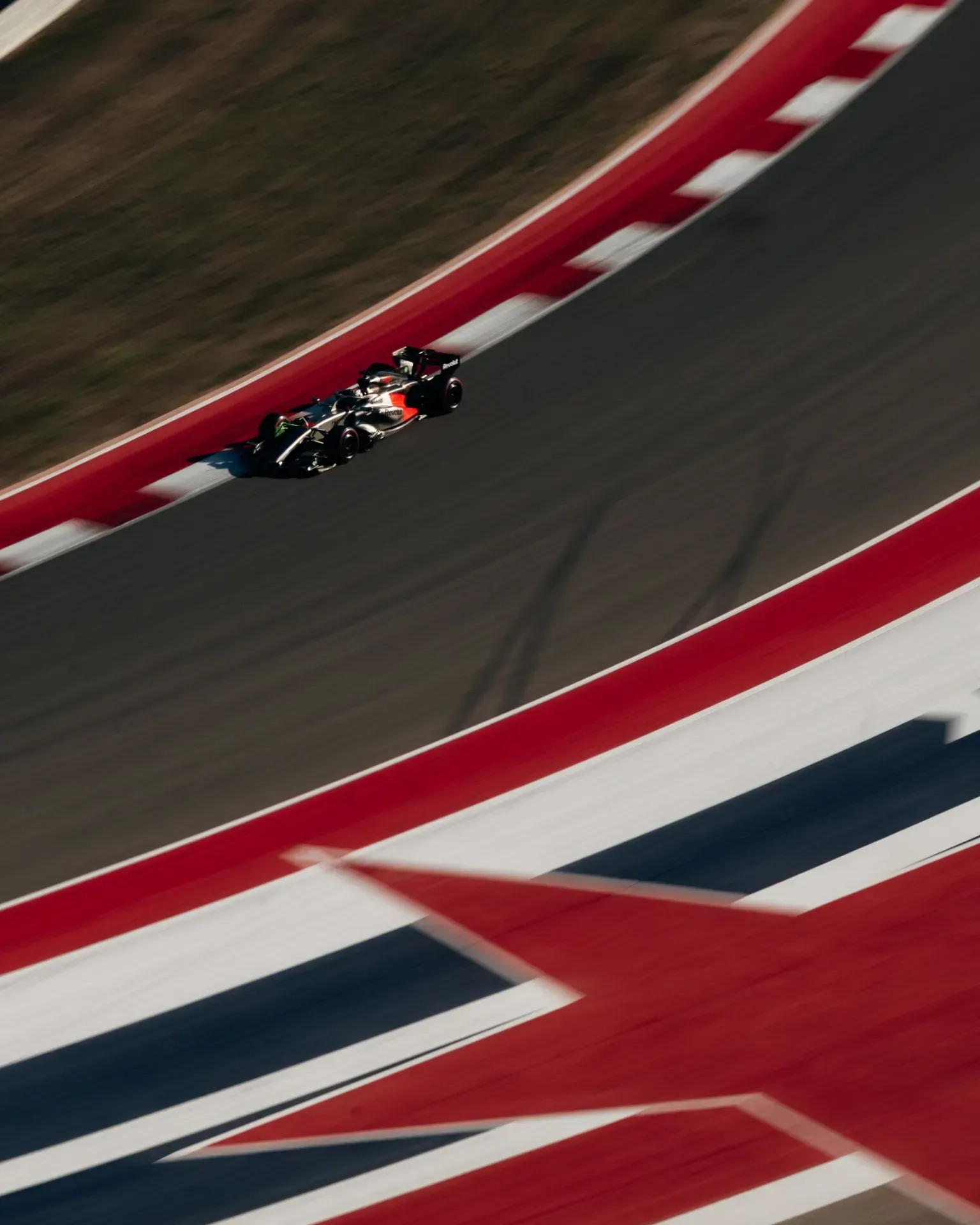 Car of the Audi Revolut F1® Team on track seen from above, with red and white kerbs and a painted flag design in foreground