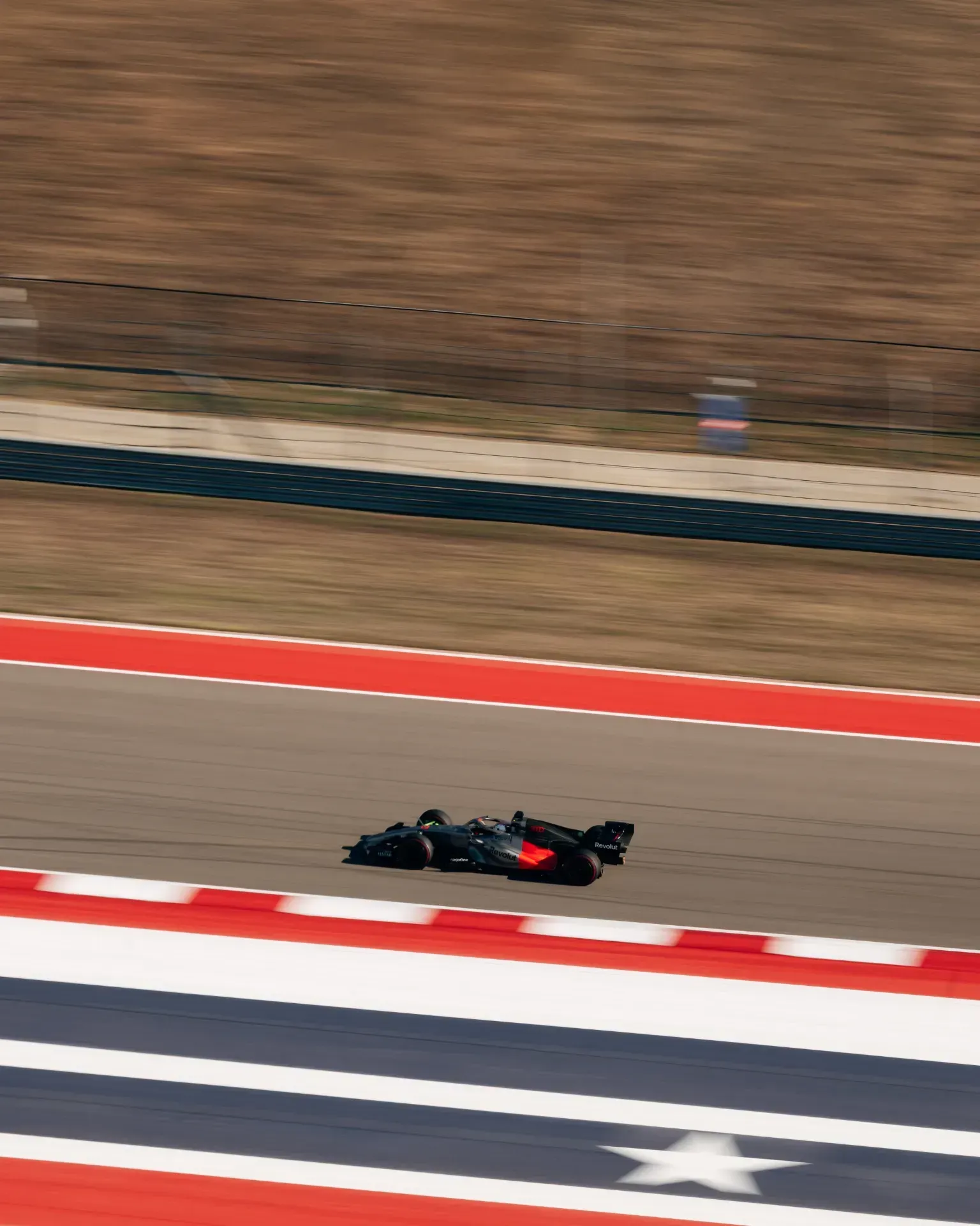 Dark car of the Audi Revolut F1® Team with red accents driving past red and white kerbs and a star marking on the track