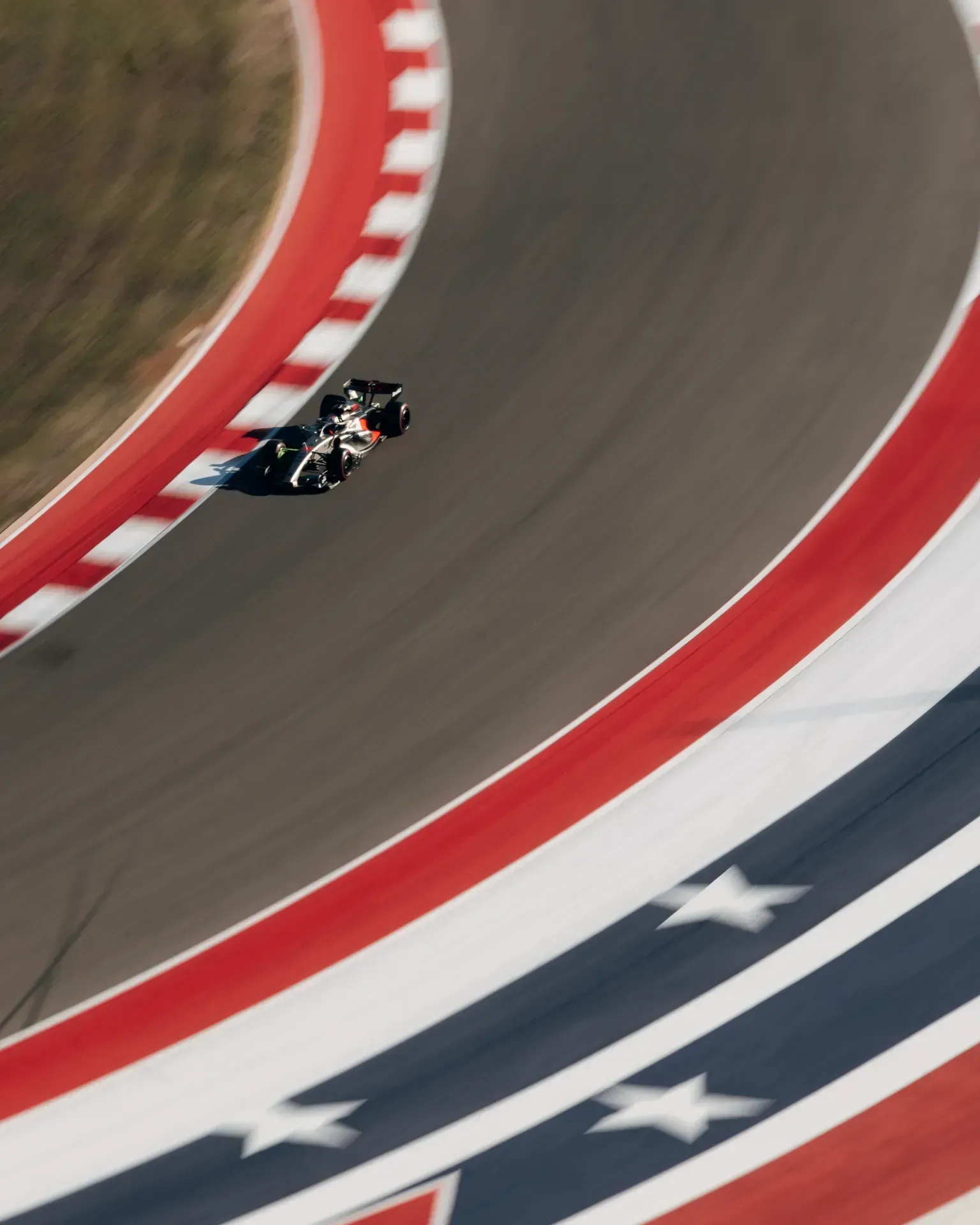 Car of the Audi Revolut F1® Team with red accents driving past red and white kerbs and a star marking on the track
