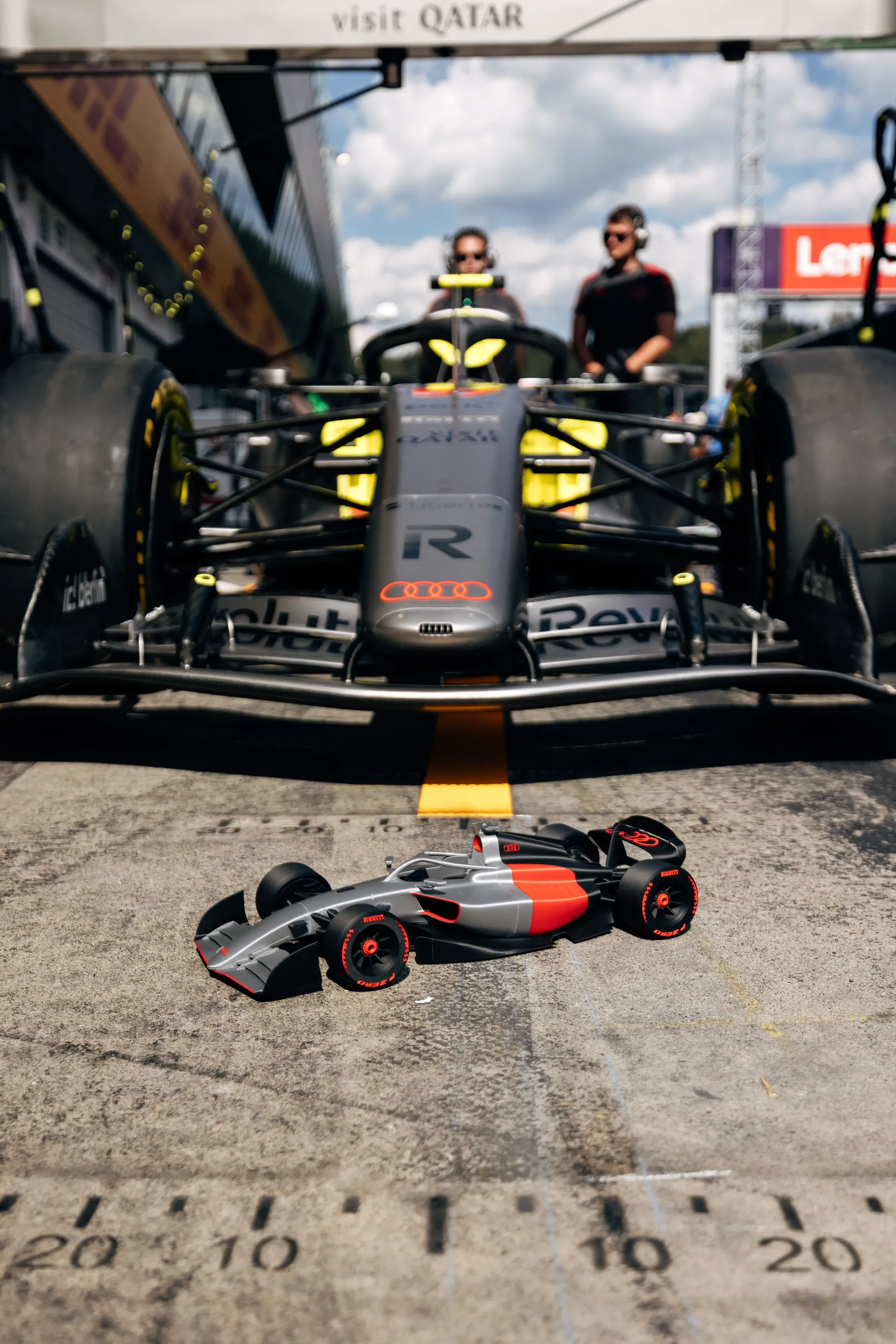An Audi Revolut F1® Team pit stop practice setup is displayed in front of the R26, with a miniature replica of the car positioned in the foreground, ahead of the Formula 1® Austrian Grand Prix at the Red Bull Ring."