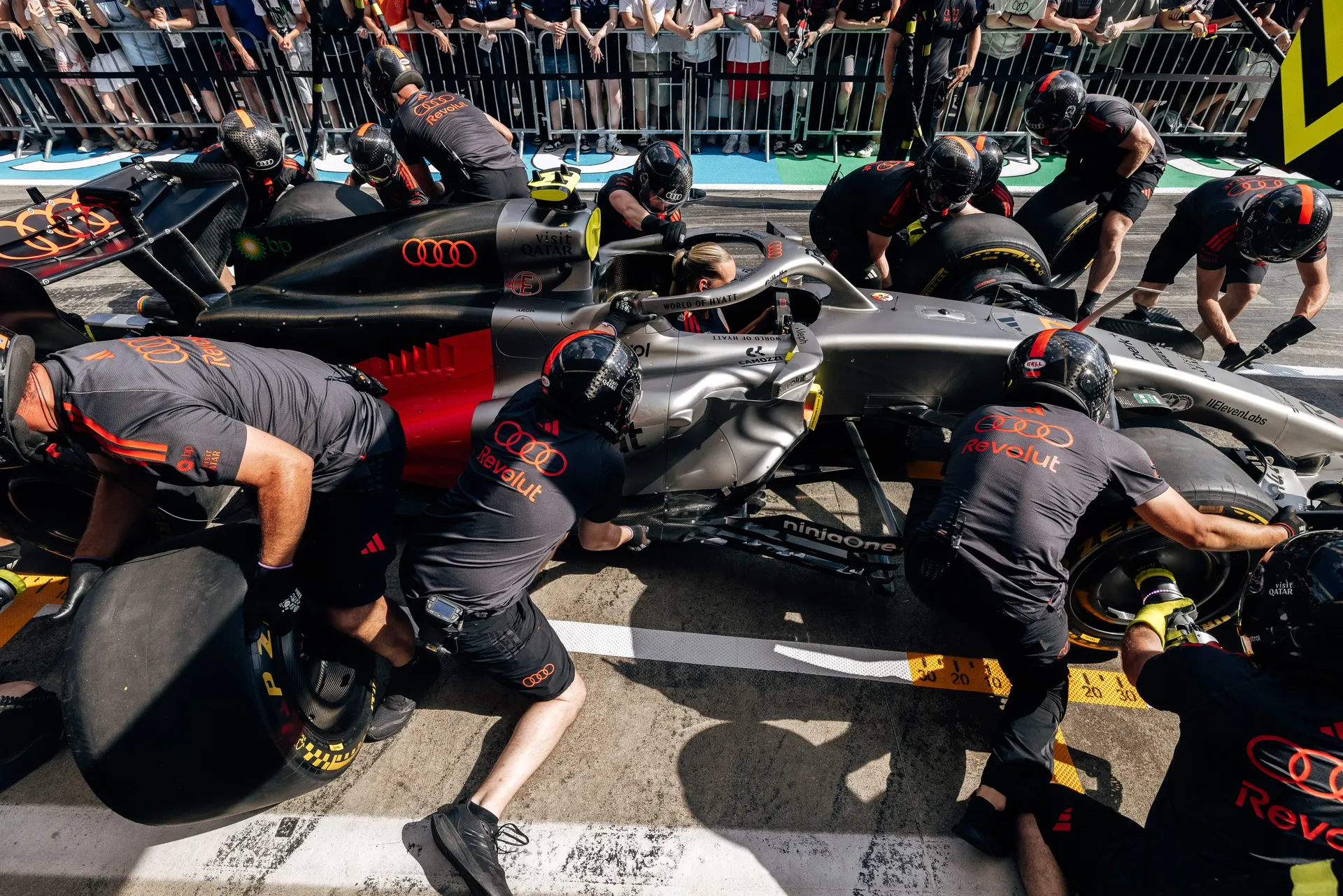 Audi Revolut F1® Team pit stop crew members surround the car during a full pit stop practice ahead of the Formula 1® Austrian Grand Prix at the Red Bull Ring.