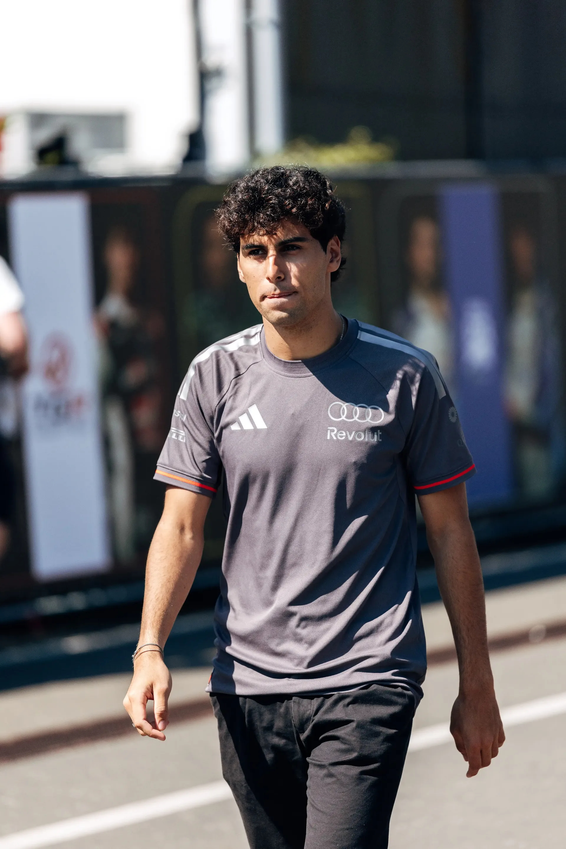 Gabriel Bortoleto driver at the Audi Revolut F1® Team walks through the paddock, with team facilities blurred in the background.