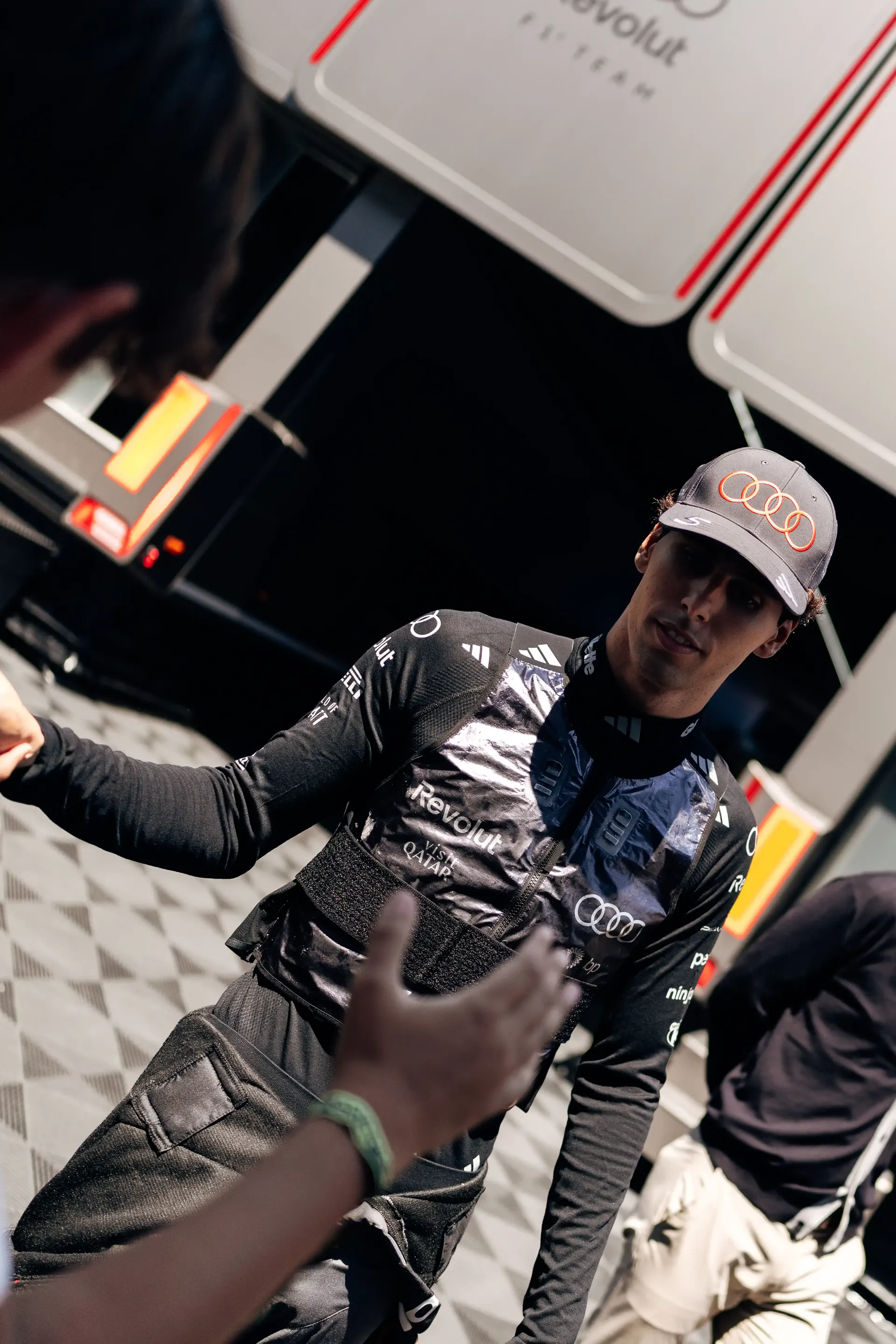 Gabriel Bortoleto, driver for the Audi Revolut F1® Team, wearing a team race suit and cap in the Formula 1 garage during FP3 at the Austrian Grand Prix in Spielberg, greeting a team member.