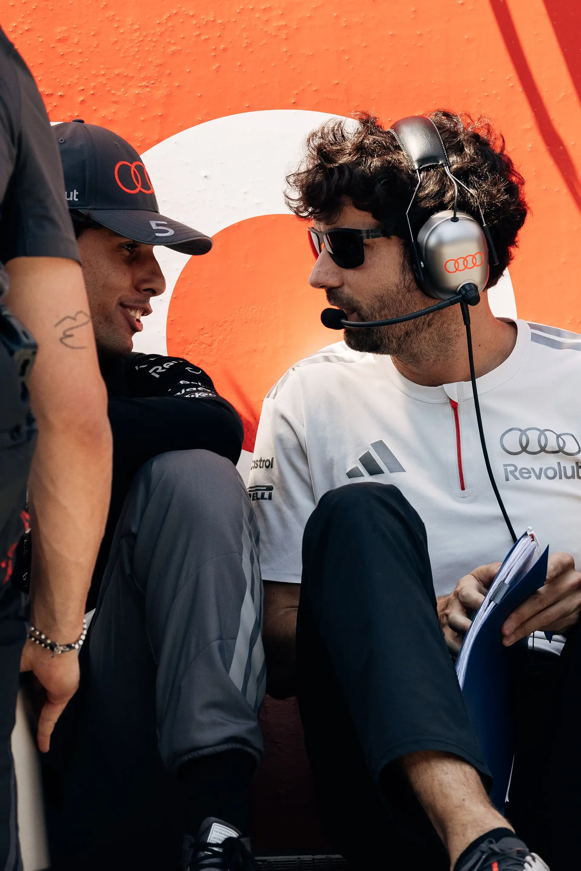 Gabriel Bortoleto driver at the Audi Revolut F1® Team chats with engineer wearing white team shirts and headsets review race information together.