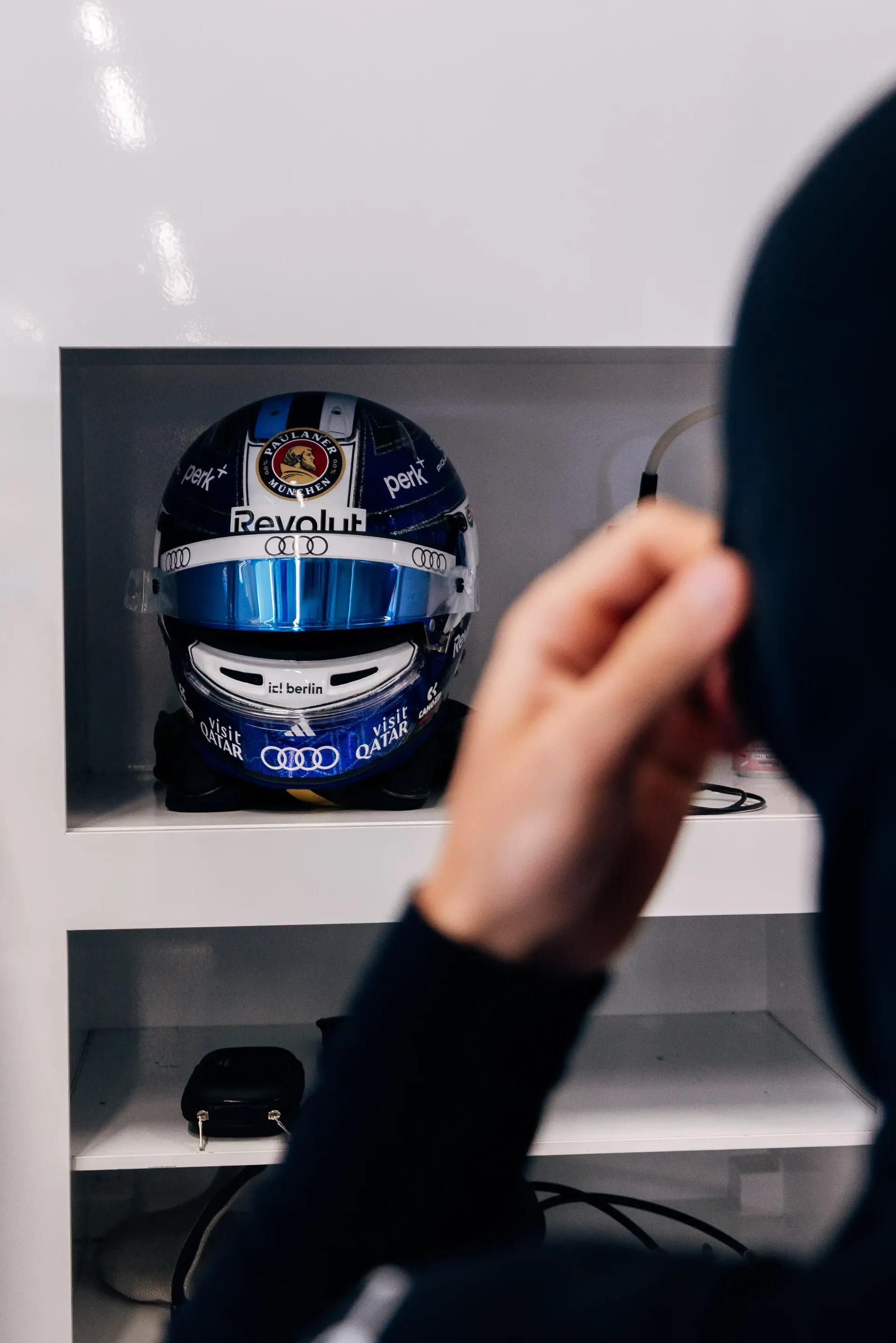 Audi Revolut F1® Team driver Paul Aron’s helmet is displayed in the garage during FP1 at Spielberg, stored in a bay as mechanics and team members prepare for track activity.
