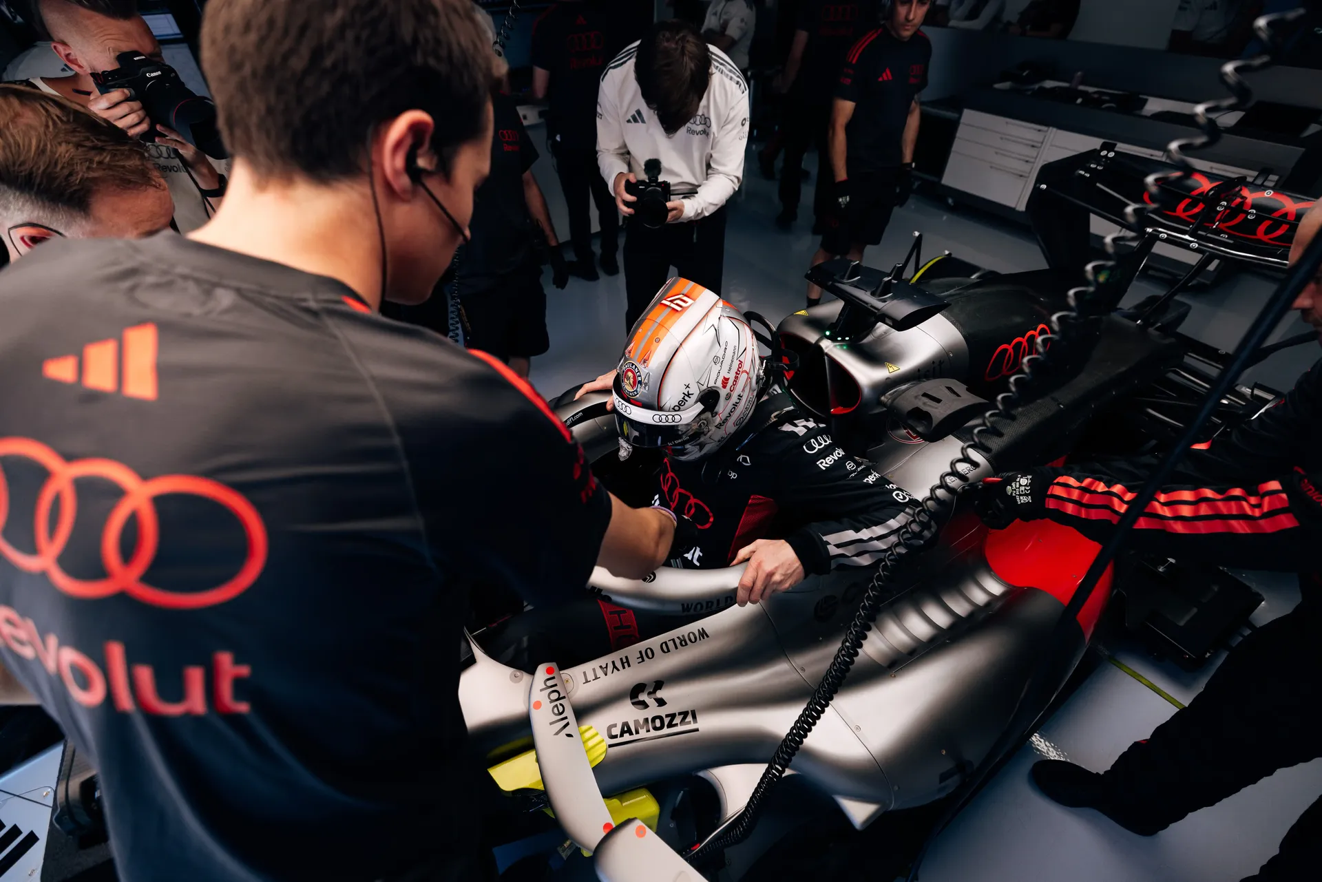Audi Revolut F1® Team mechanics working on the car in the garage during FP1 at Spielberg, with detailed focus on cockpit and steering wheel setup before track running.