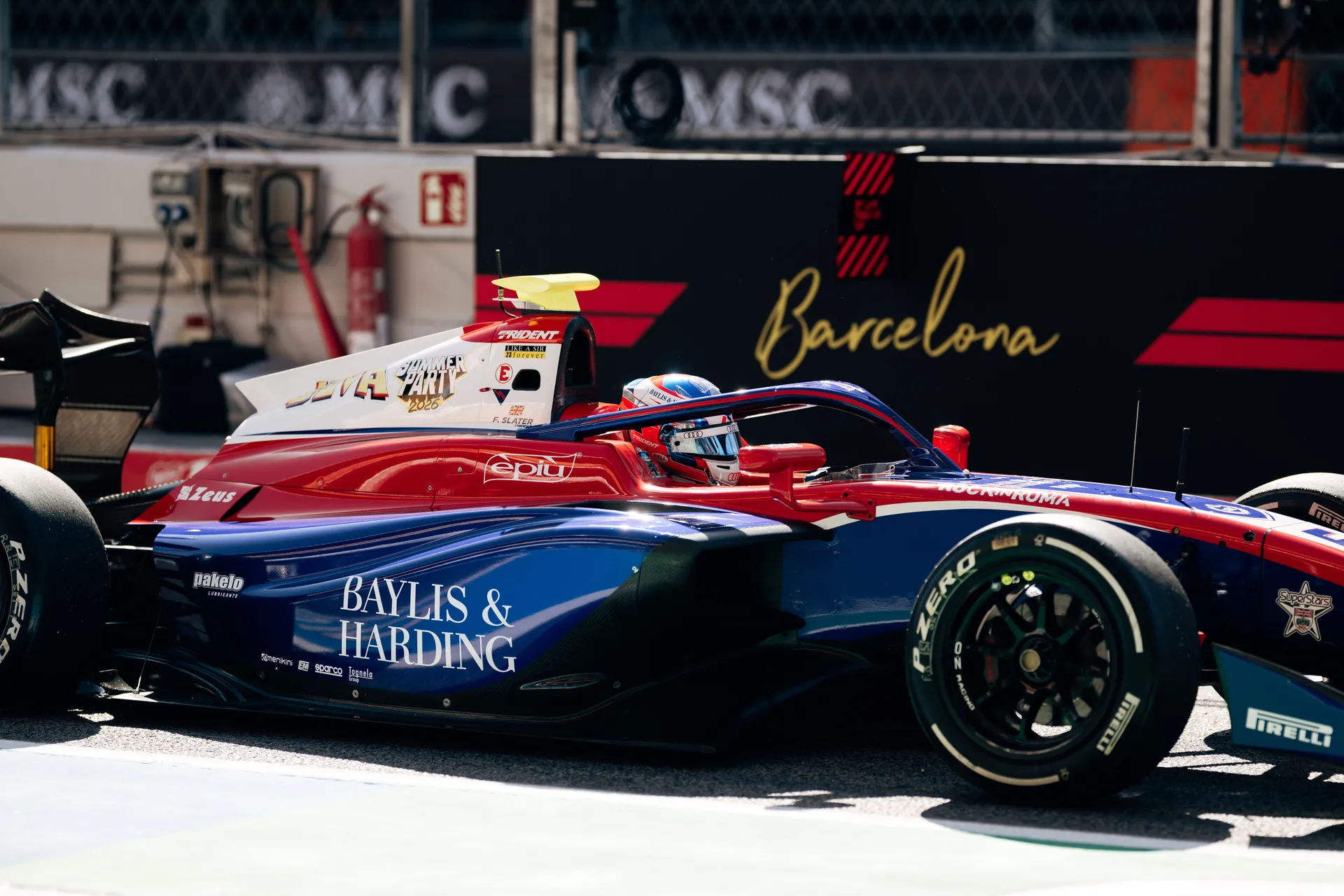 Freddie Slater driving an F3 car in Barcelona, captured side-on in the pit lane with team branding visible on the car.