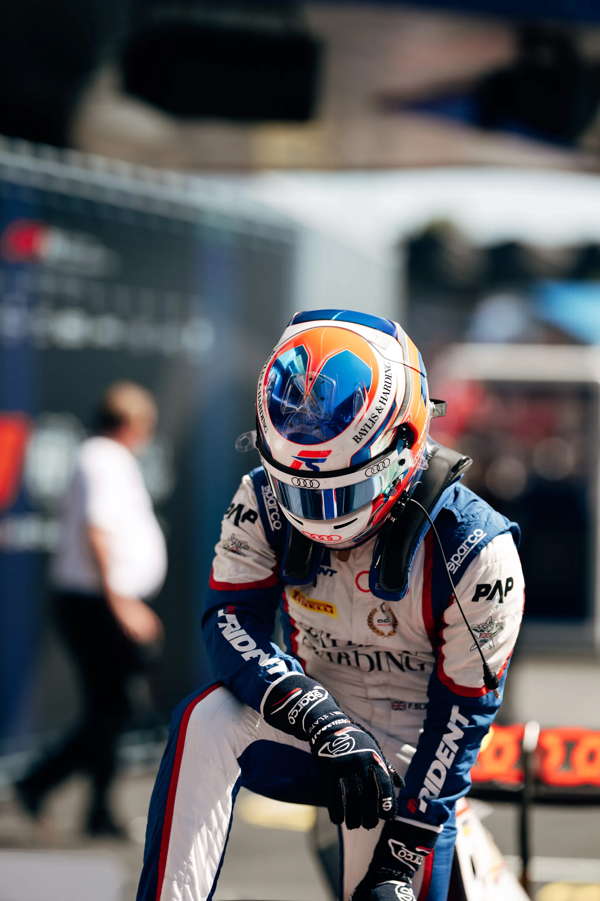 Freddie Slater kneeling beside his F3 car in full race suit and helmet, focused during pre-race preparations in the paddock.