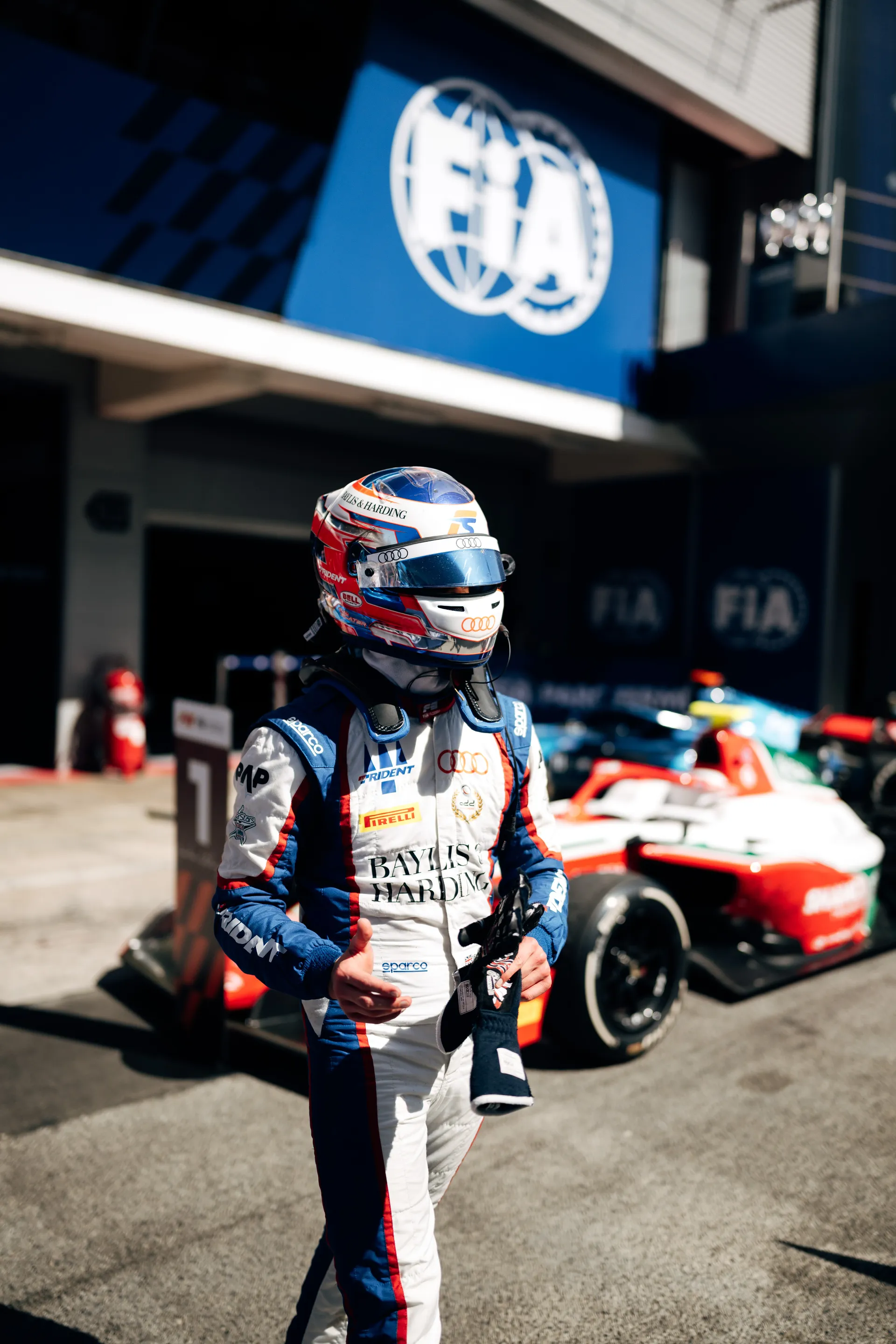 Freddie Slater walking in full race gear and helmet past FIA signage, holding his gloves after the session in Barcelona.
