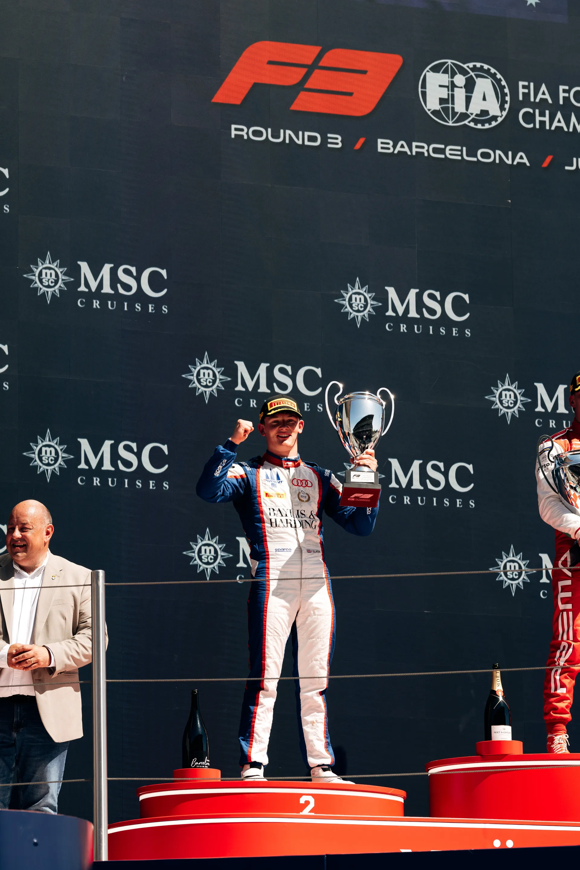 Freddie Slater celebrating on the podium in Barcelona, raising a trophy after finishing second in the F3 sprint race.