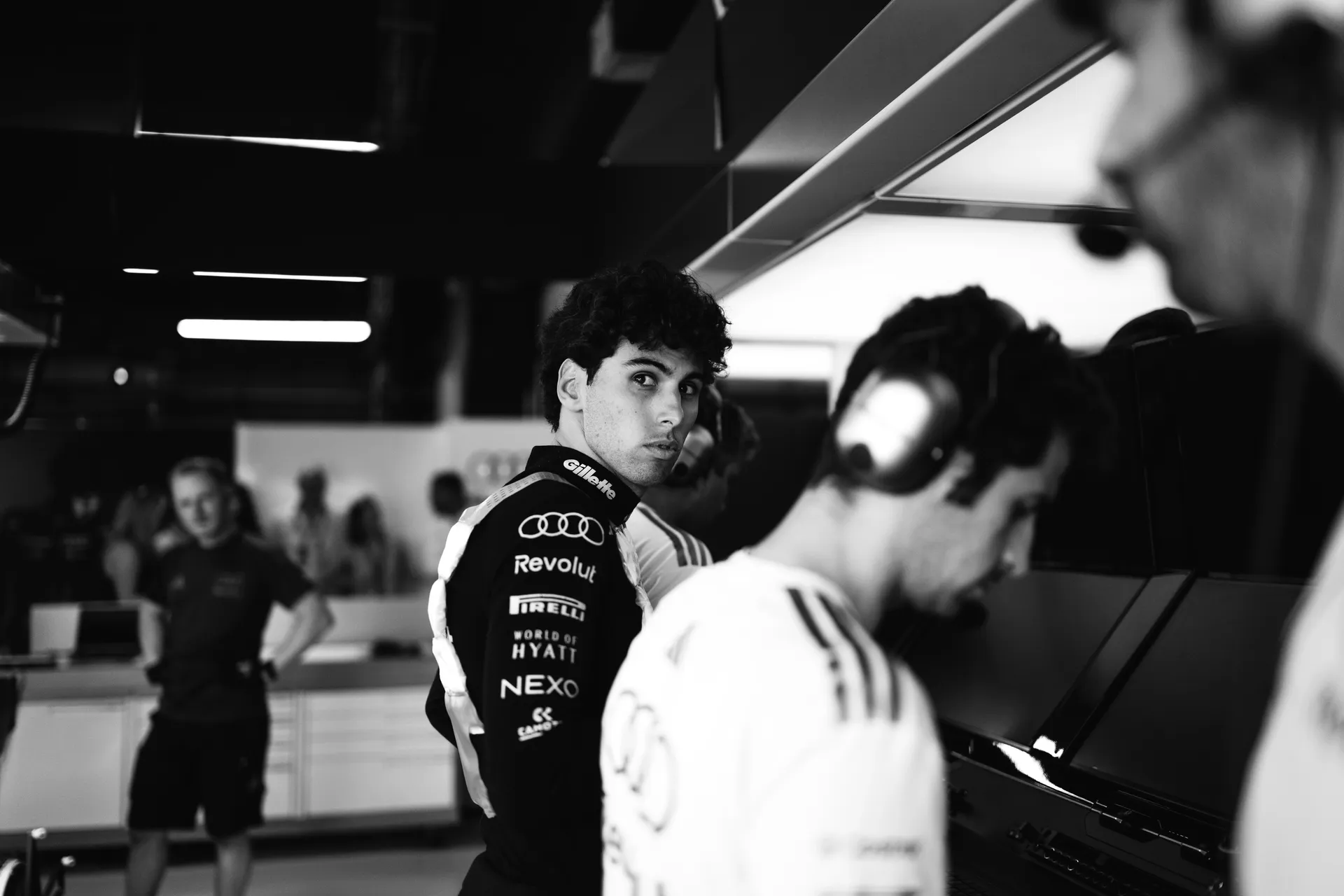 Gabriel Bortoleto looks over his shoulder inside the Audi Revolut F1® Team garage while engineers work on computers in the foreground