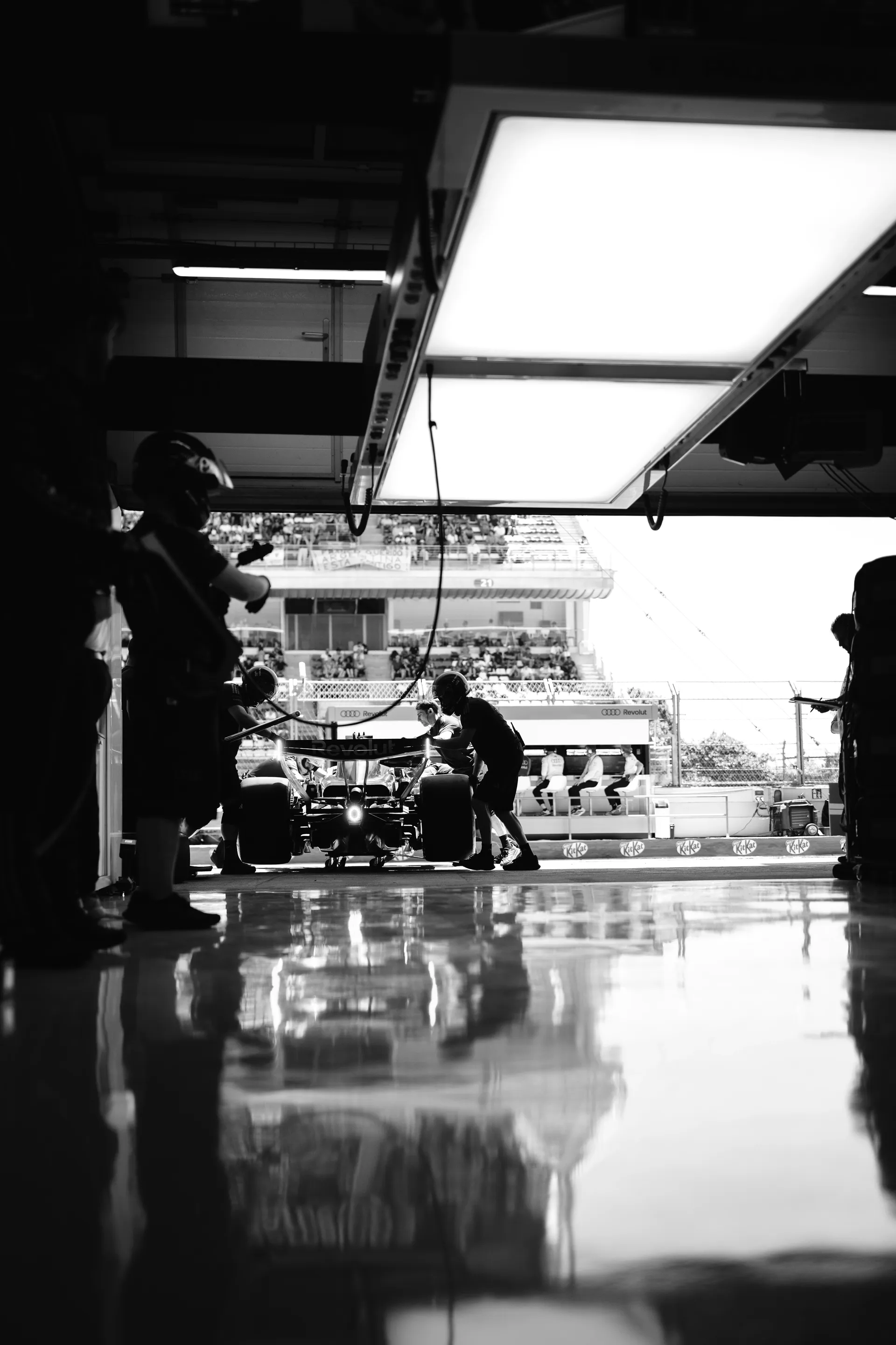 Silhouetted Audi Revolut F1® Team pit crew pushing a Formula One car out of the garage, captured in high-contrast black and white.