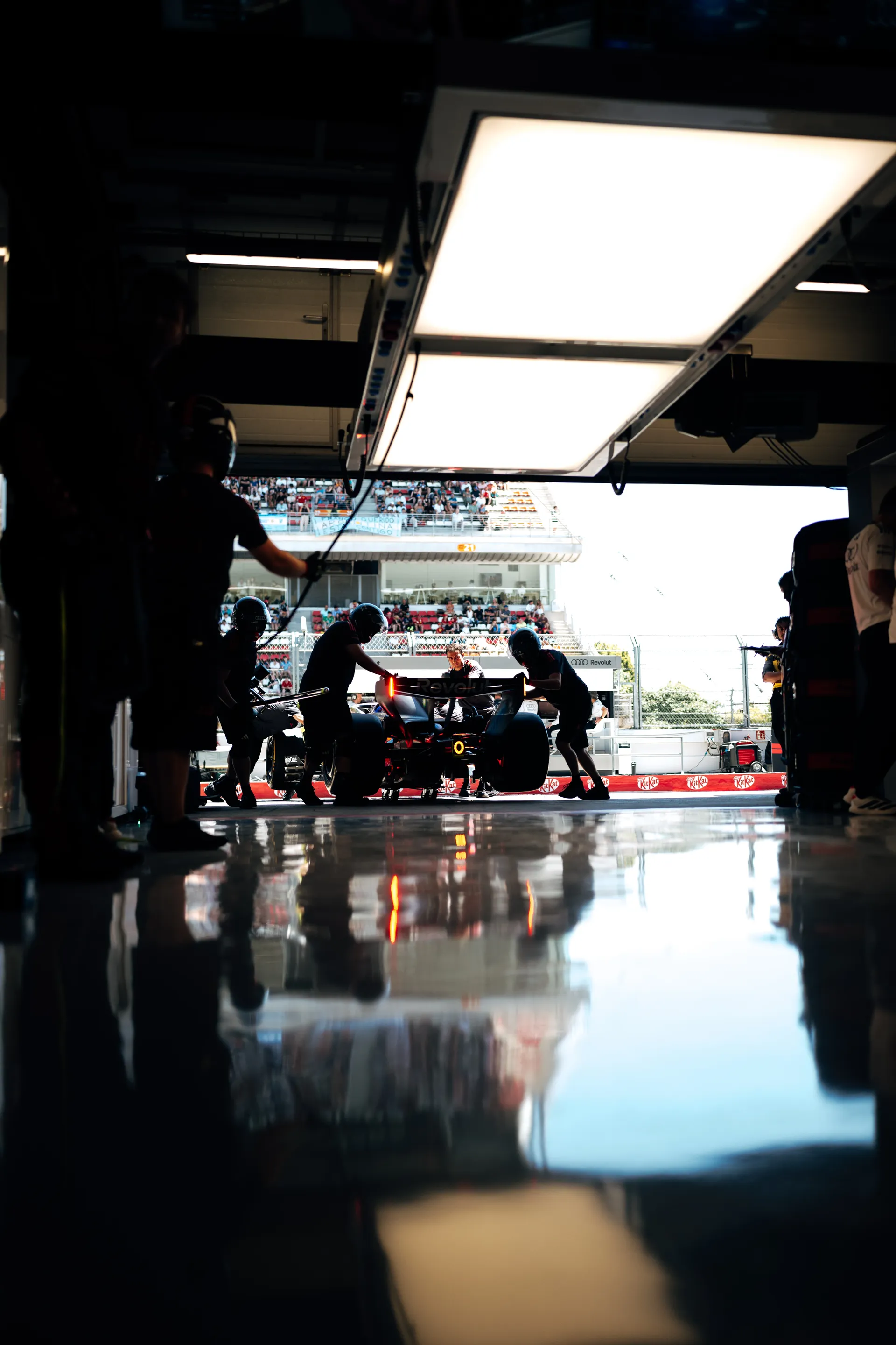 Rear view of an Audi Revolut F1® Team car being rolled out of the garage, with glowing rear light reflected on the polished pit floor.