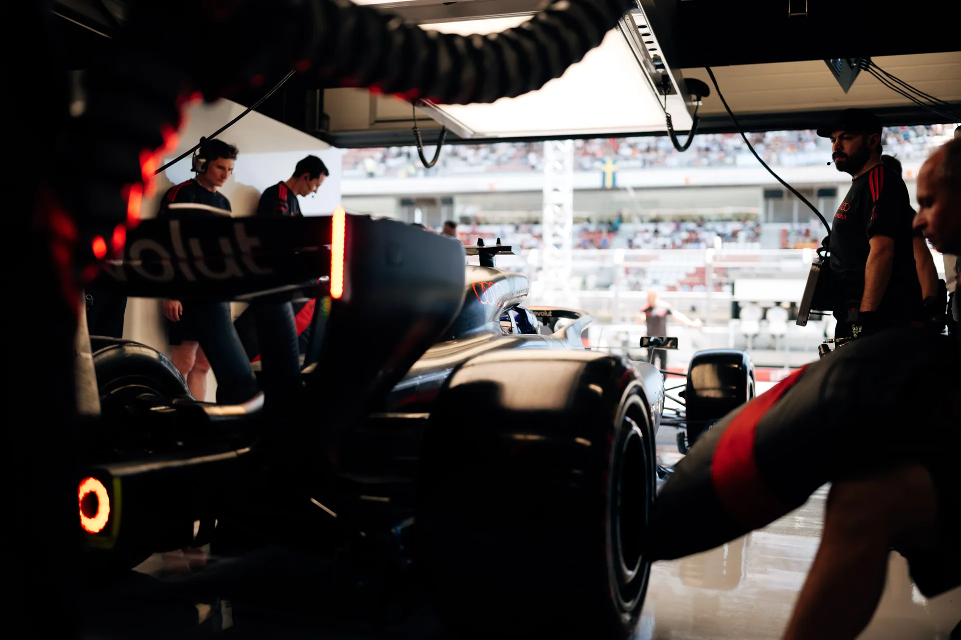 Low-angle view of an Audi Revolut F1® Team car positioned at the garage exit, surrounded by engineers and mechanics preparing for release.
