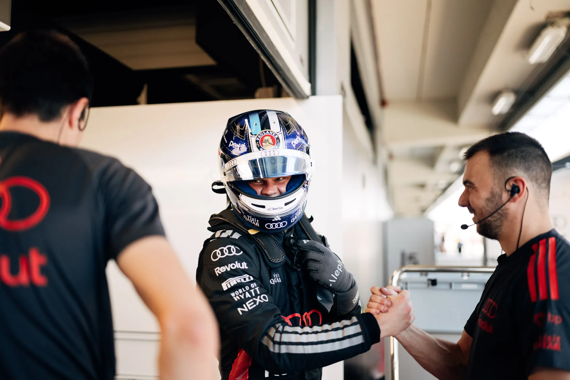 Audi Revolut F1® Team driver Paul Aron in full race gear greeting a crew member with a handshake inside the garage.