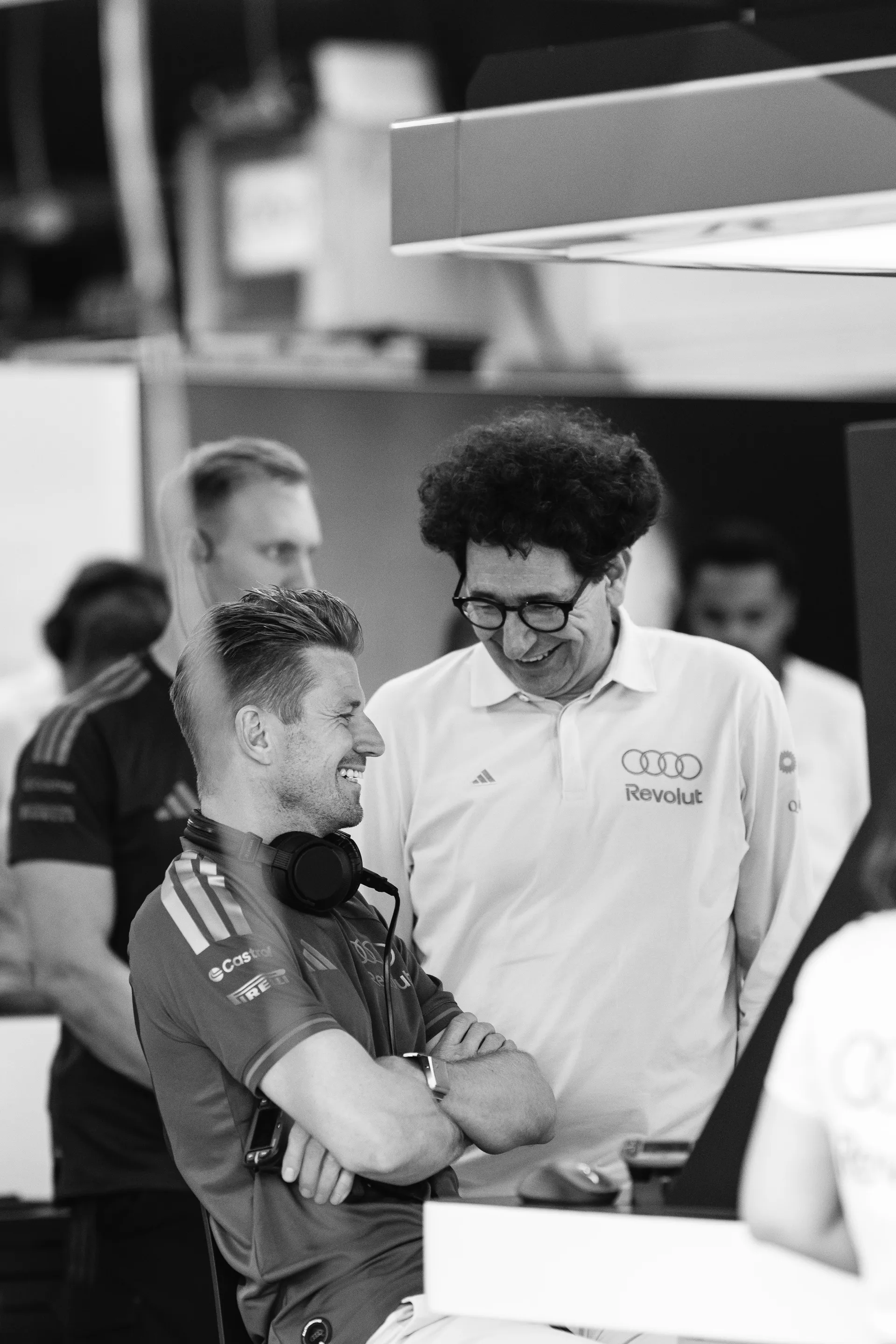 Mattia Binotto smiling while talking to Nico Hulkenberg in the garage, captured in a candid black and white moment.