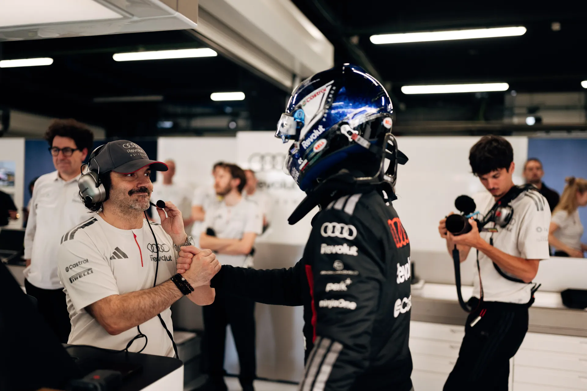 Paul Aron in full race gear greeting a team member with a handshake inside the Audi Revolut F1® Team garage.