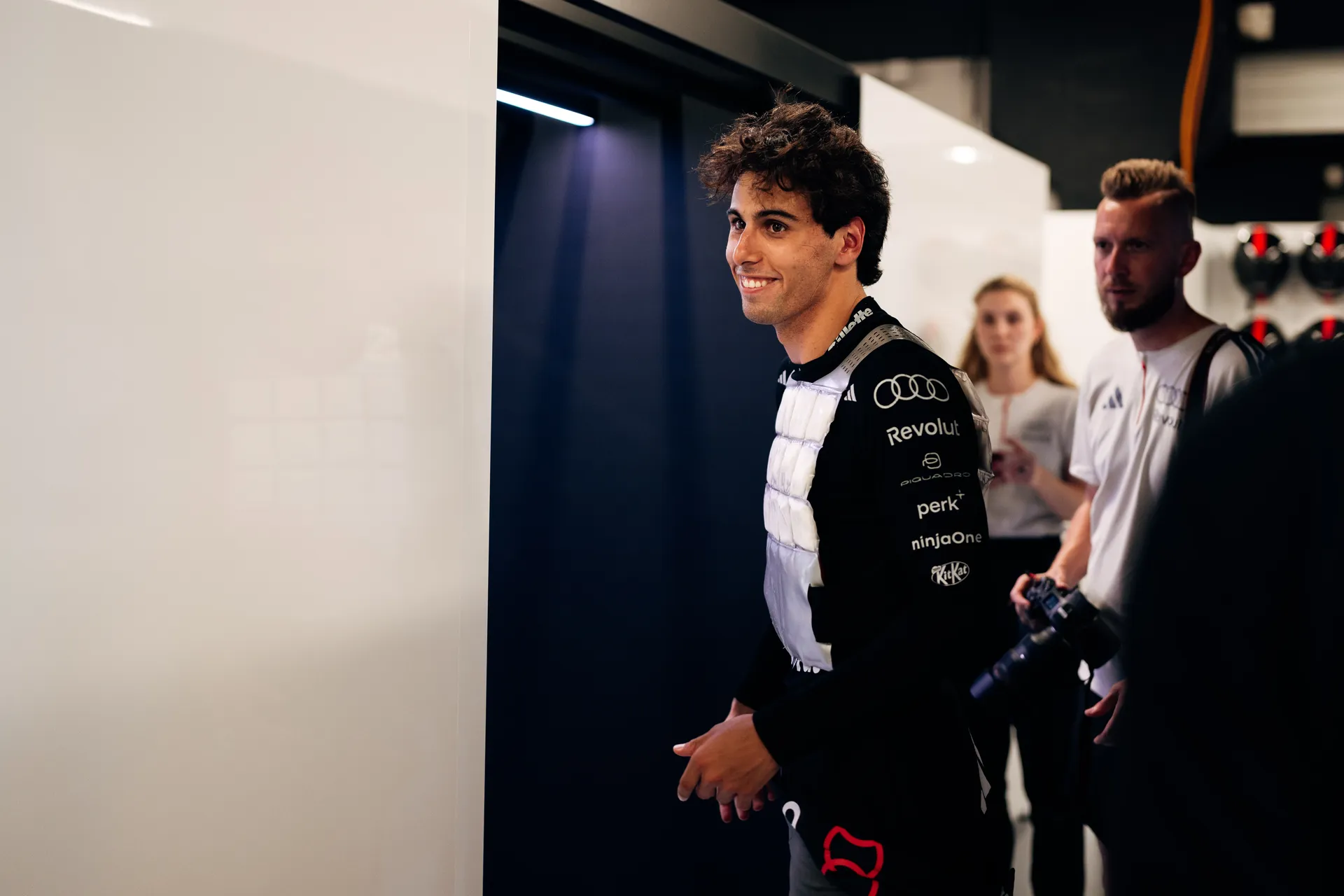 Gabriel Bortoleto walking through the garage wearing protective vest gear, looking focused ahead.