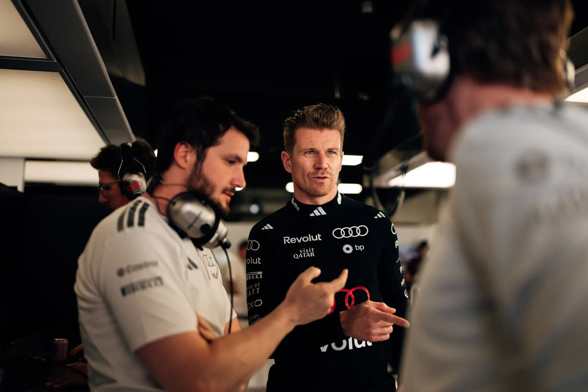 Nico Hulkenberg discussing with Audi Revolut F1® Team engineers in the garage, gesturing during a technical conversation.