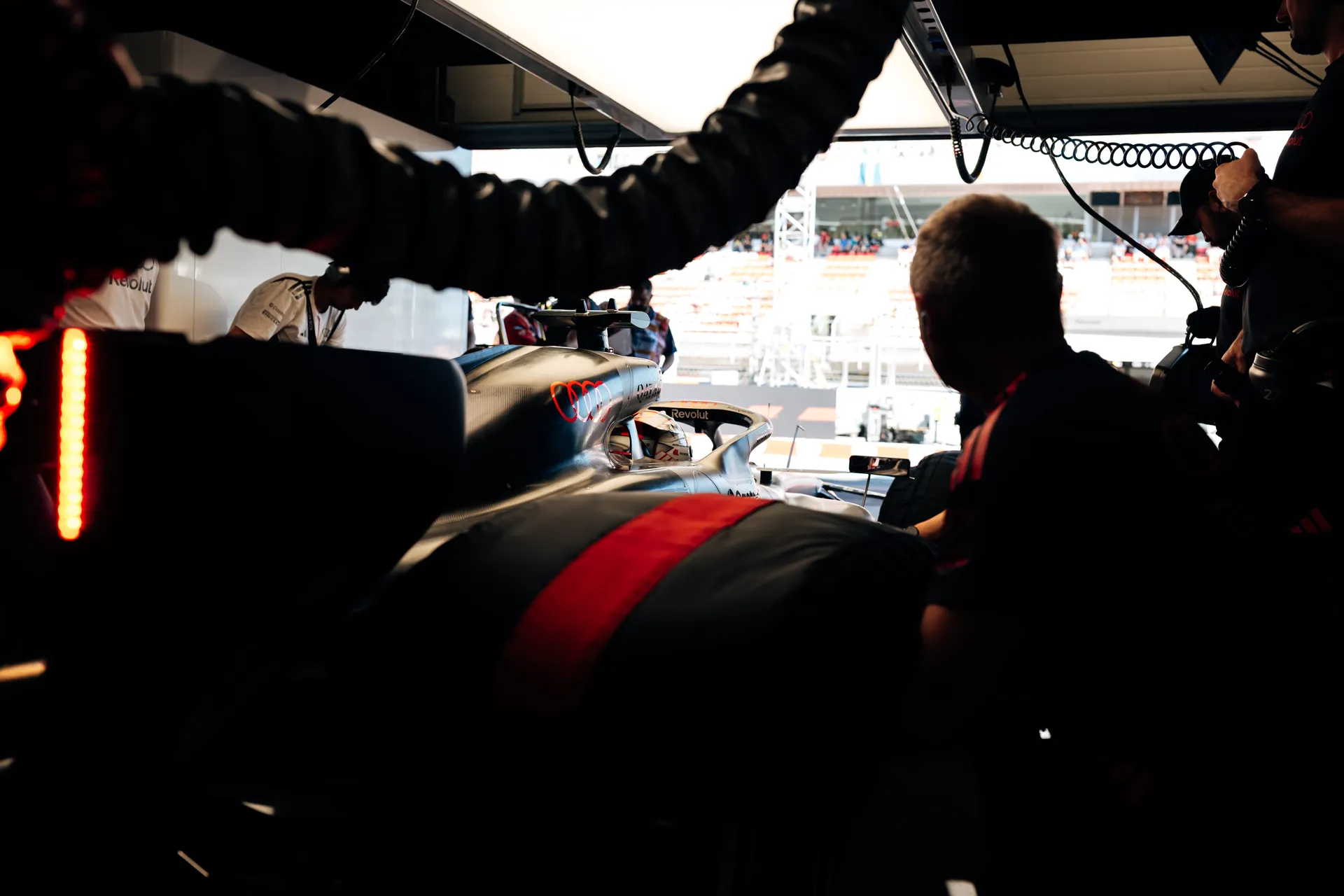 Audi Revolut F1® Team mechanics preparing the car inside the garage, with pit lane visible outside and equipment surrounding the cockpit.