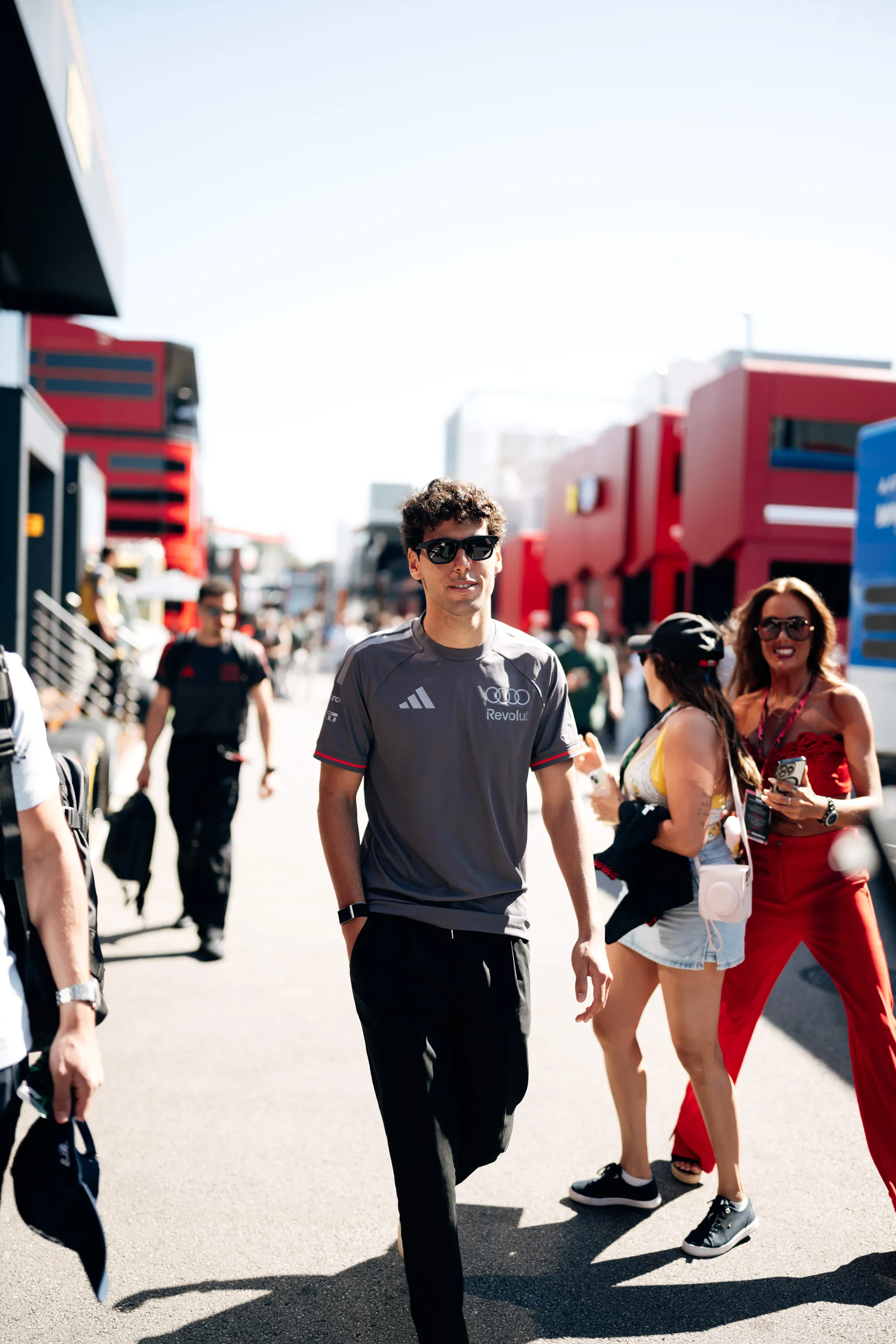 Gabriel Bortoleto walking through the paddock at Circuit de Barcelona-Catalunya wearing Audi Revolut F1® Team kit, with fans and team structures in the background