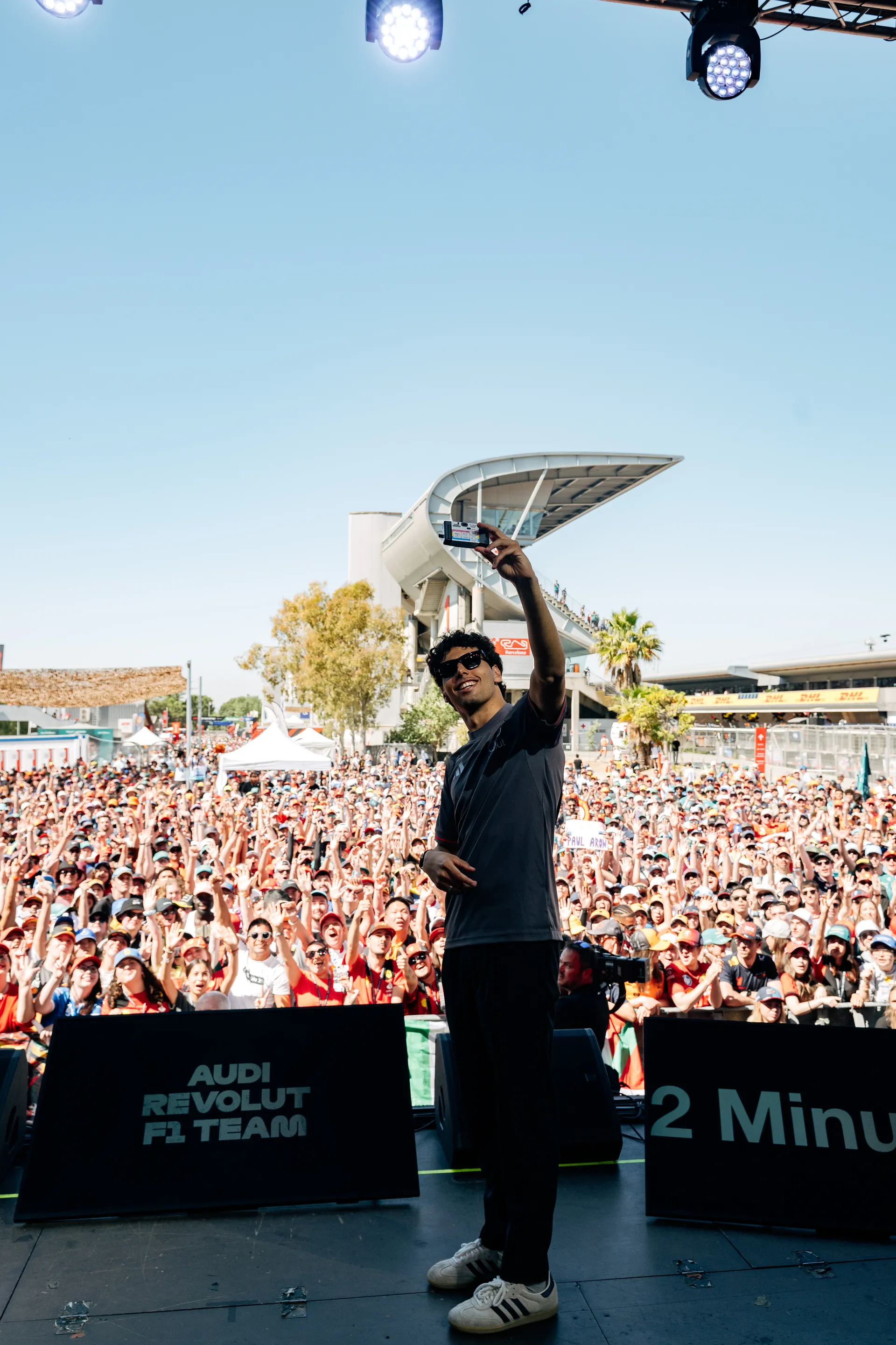 Gabriel Bortoleto taking a selfie on stage in front of a large crowd of fans during a public fan event at Circuit de Barcelona-Catalunya