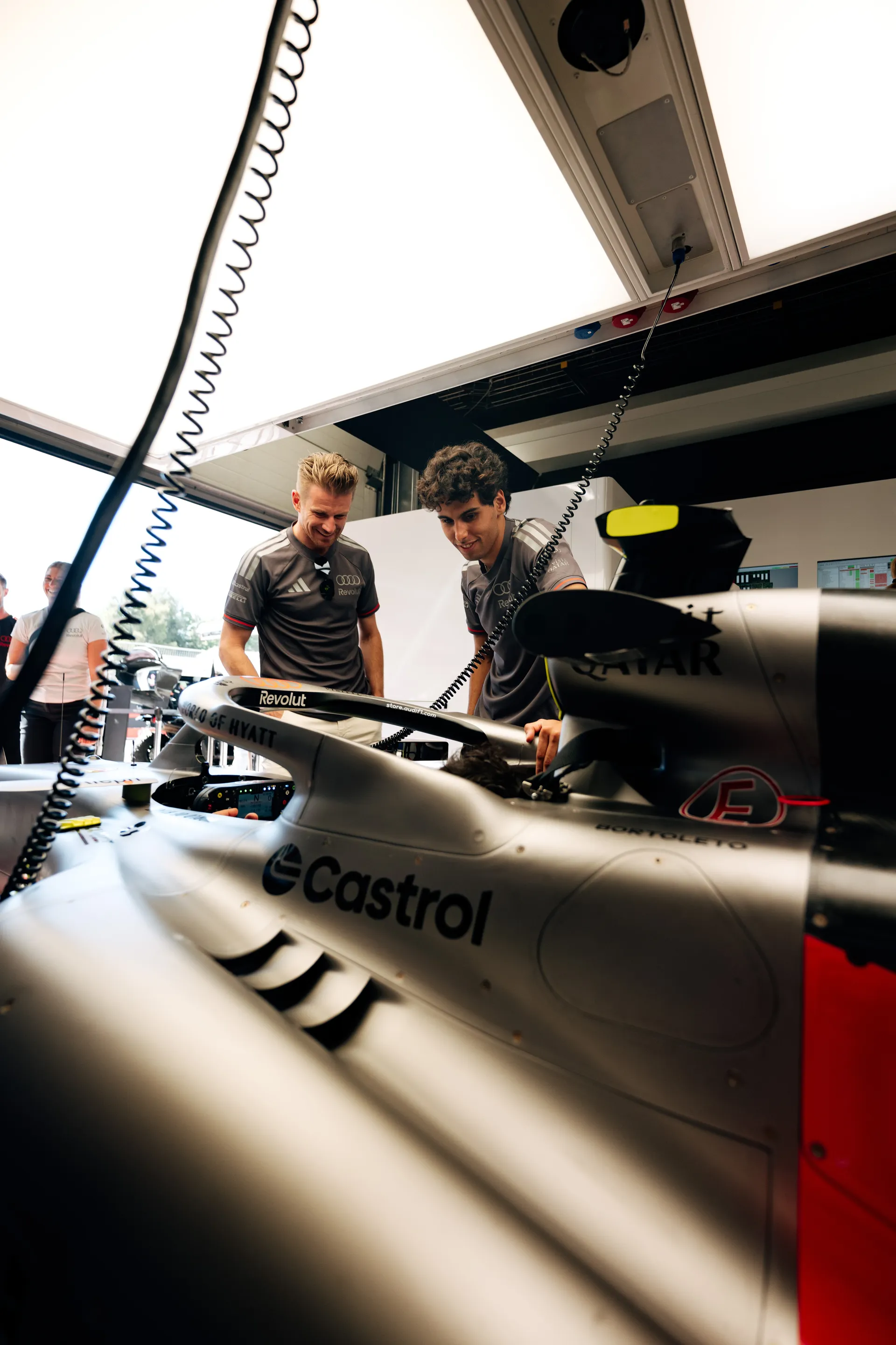 Nico Hulkenberg and Gabriel Bortoleto inspecting the Audi Revolut F1® Team car together inside the garage environment