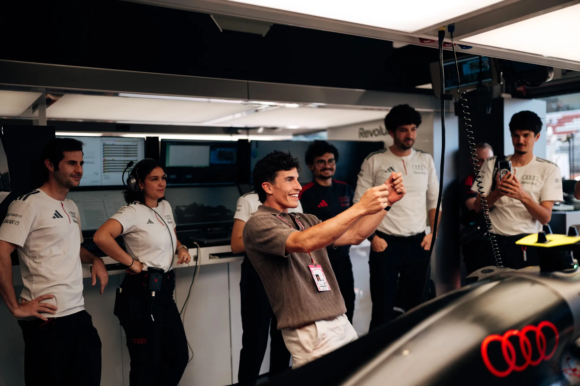 A celebrity demonstrating steering input inside the garage while Audi Revolut F1® Team members watch and record