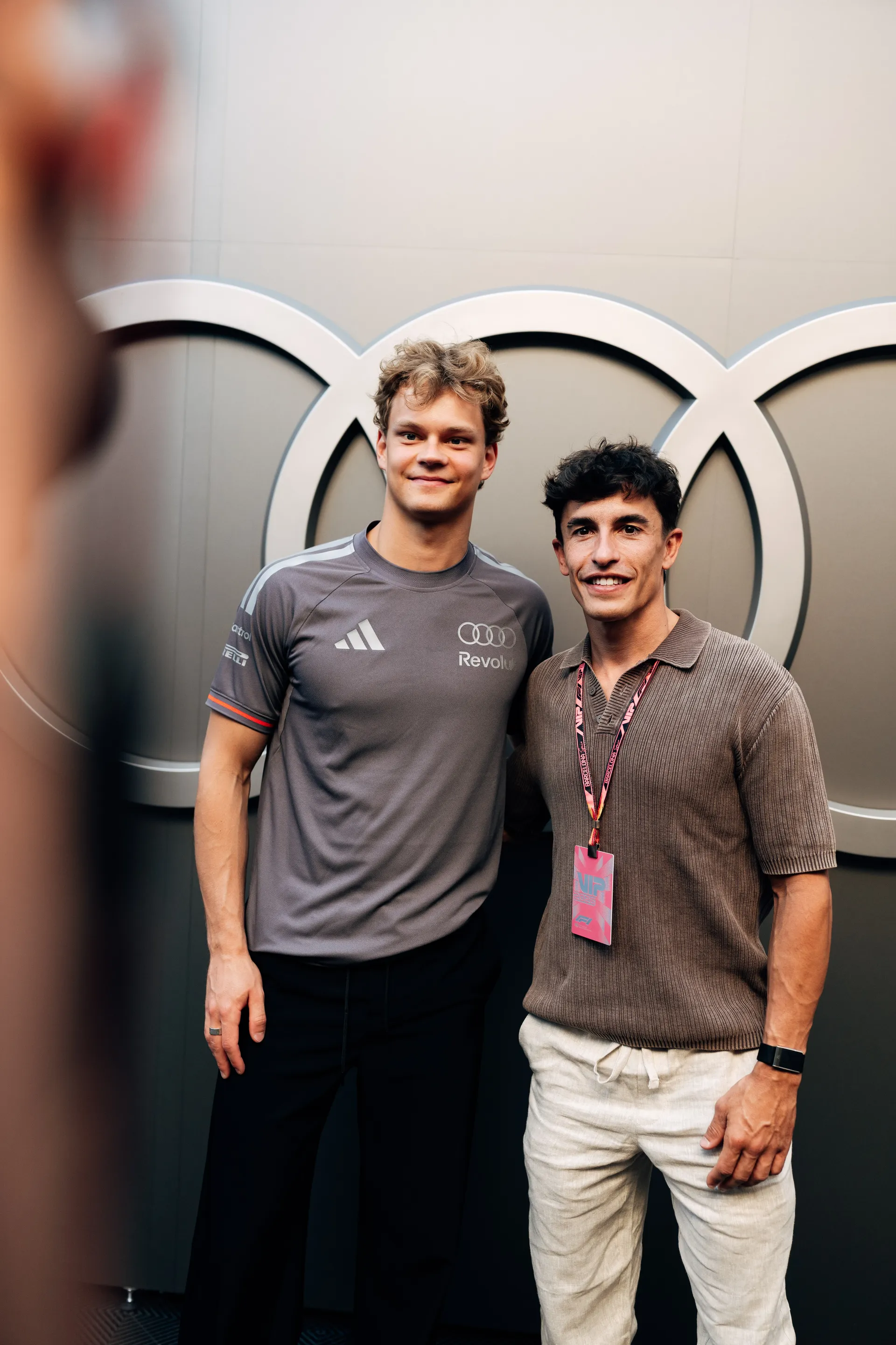 Paul Aron and Marc Márquez posing together in front of Audi rings branding in the Audi Revolut F1® Team paddock