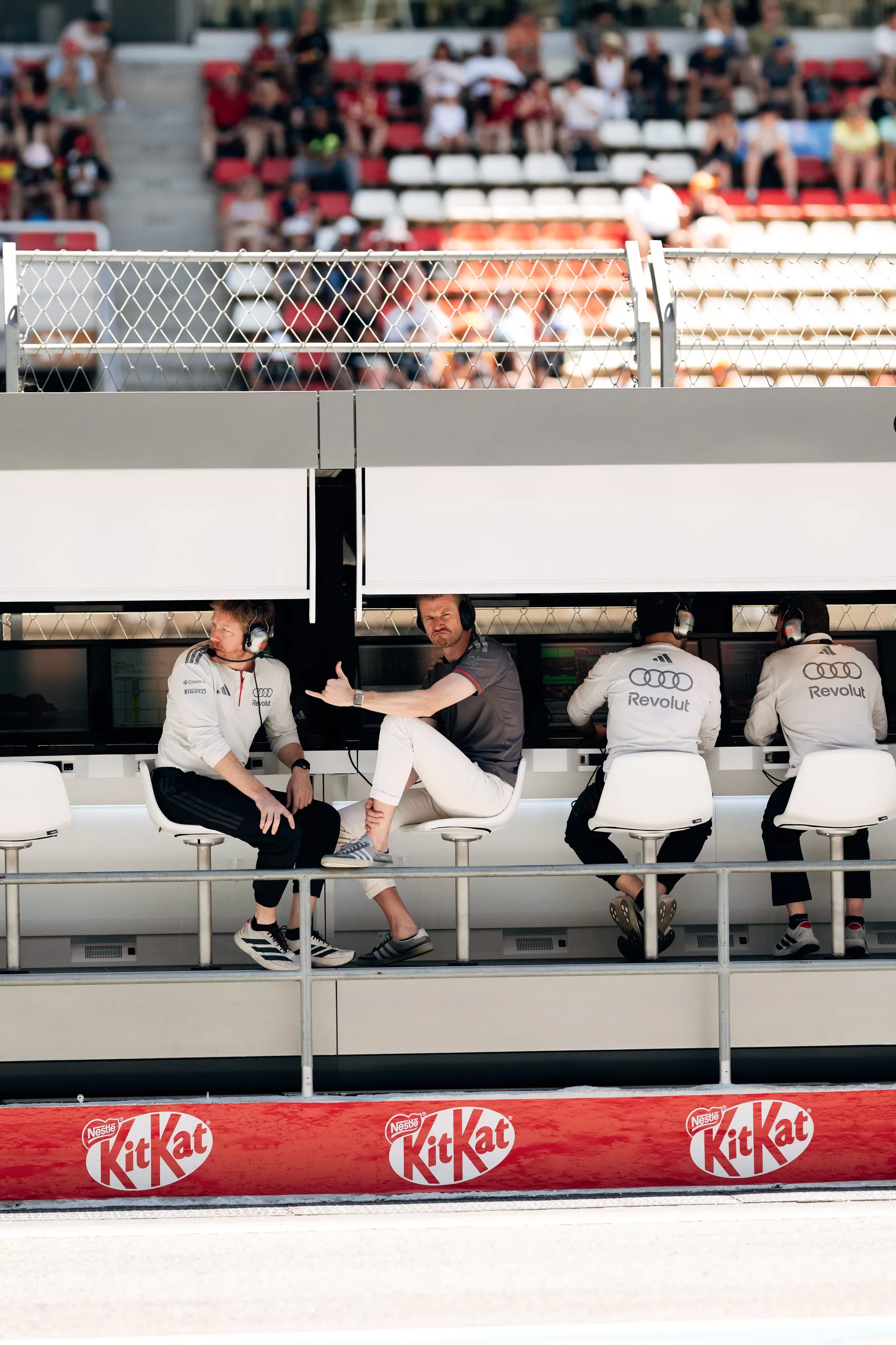 Audi Revolut F1® Team engineers and Nico Hulkenberg seated at the pit wall monitoring race data with grandstand crowd behind