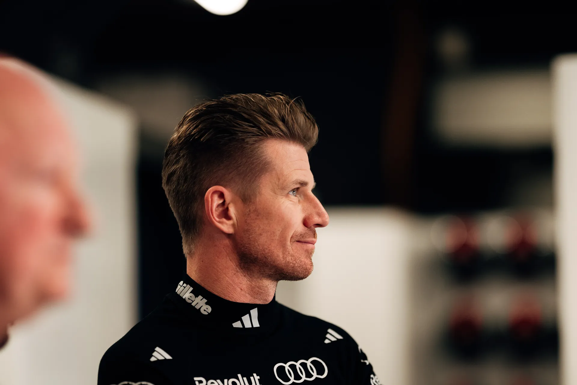 Nico Hulkenberg in side profile listening attentively during a garage discussion