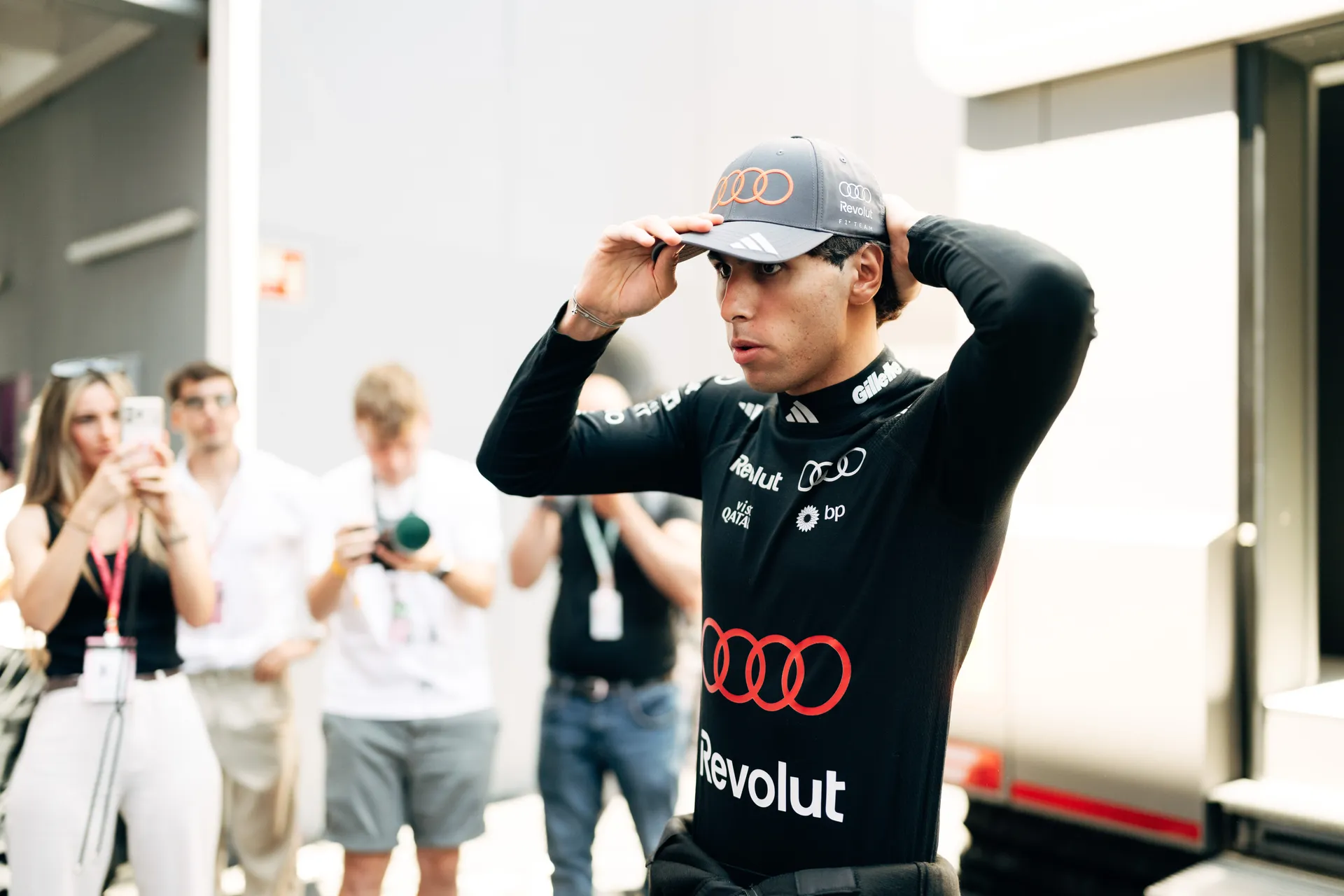Gabriel Bortoleto adjusting his Audi Revolut F1® Team cap in the paddock, surrounded by media and photographers in Barcelona