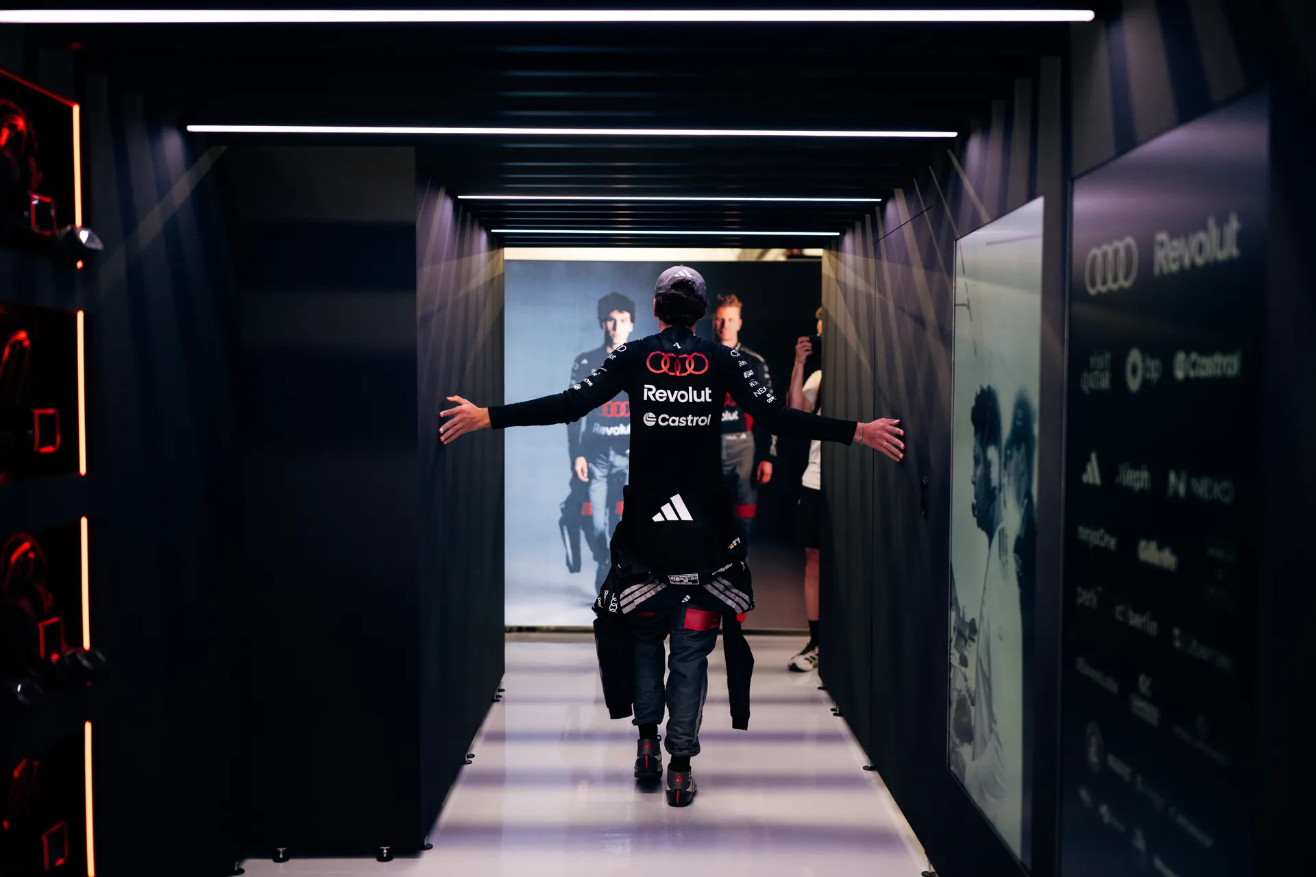 Audi Revolut F1® Team driver Gabriel Bortoleto walking through a dark garage tunnel with arms outstretched before heading to the pit lane