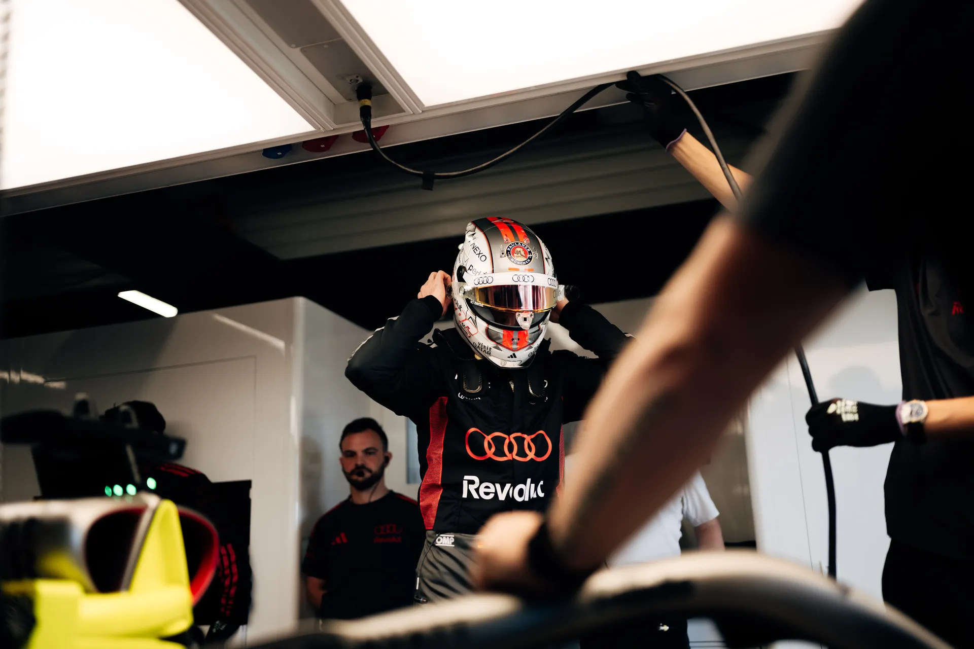 Nico Hulkenberg putting on his helmet inside the Audi Revolut F1® Team garage before a session, with mechanics preparing equipment around him