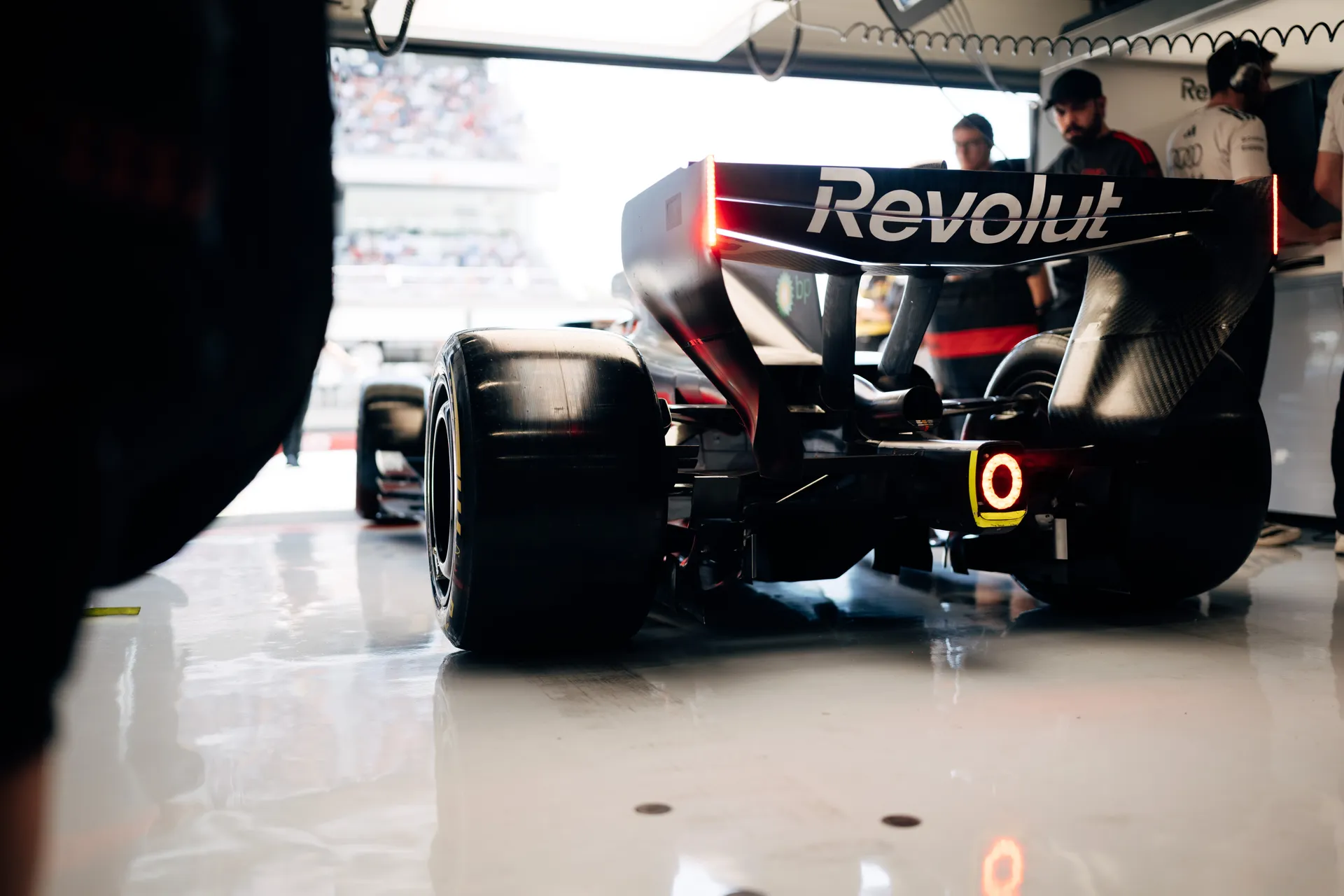 Rear view of the Audi Revolut F1® Team car in the garage with illuminated rain light, mechanics working in the background
