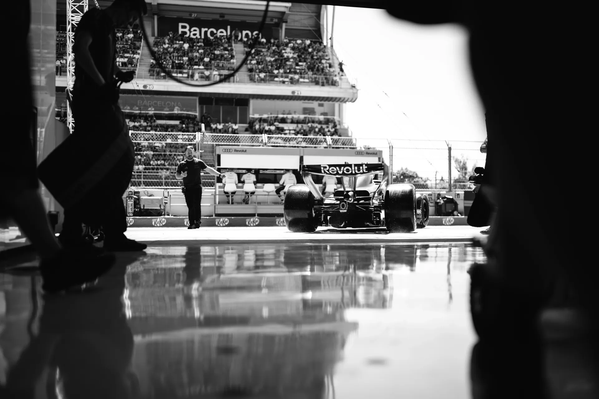 Audi Revolut F1® Team car exiting the garage into the Barcelona pit lane, framed by team members and garage shadows