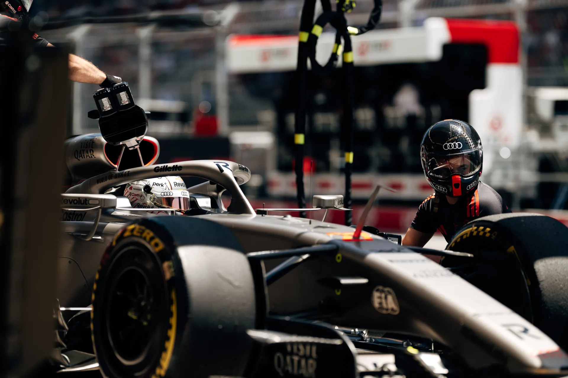 Audi Revolut F1® Team pit crew preparing the car in the pit lane, with one crew member kneeling beside the front wheel