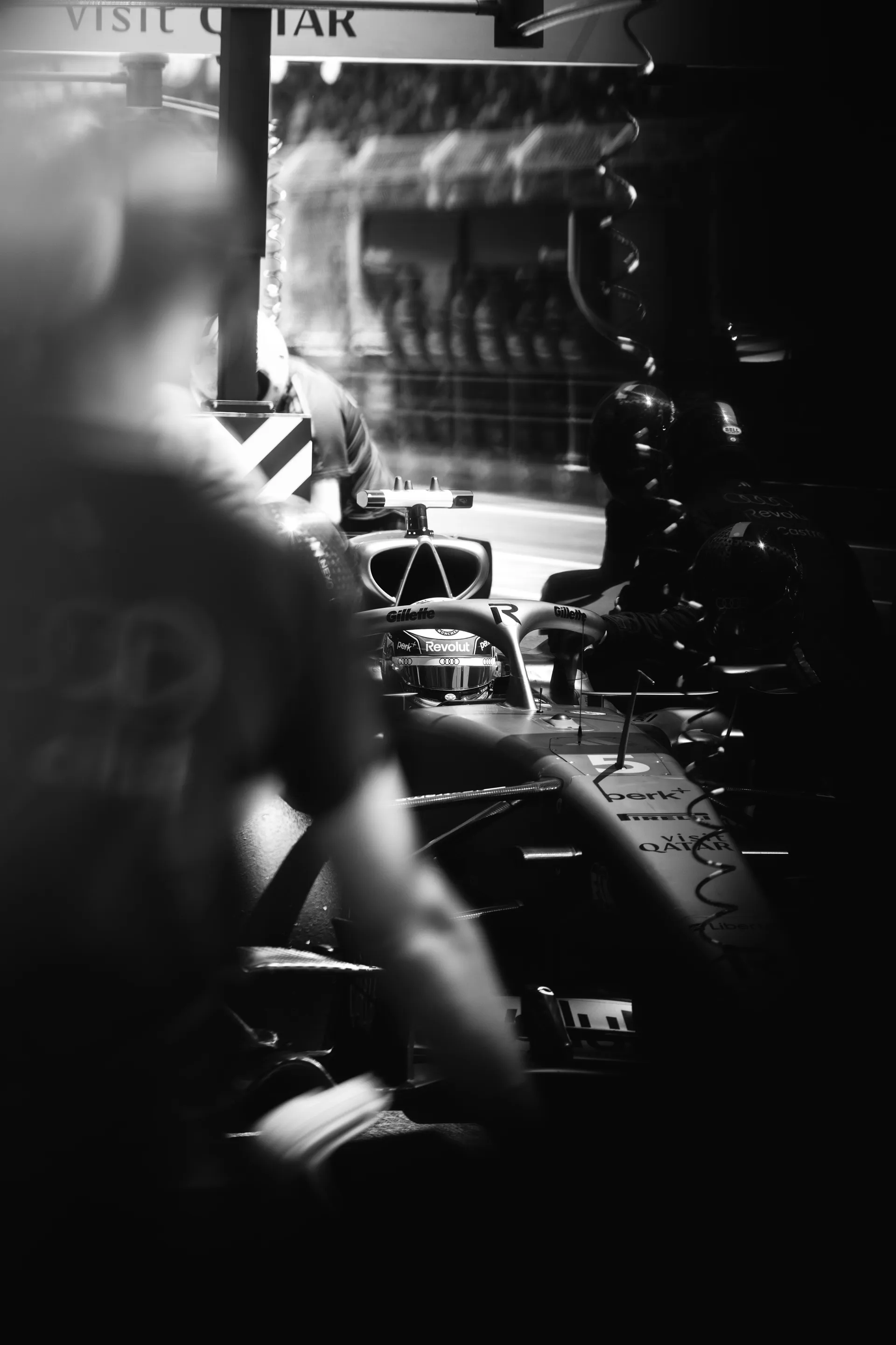 Audi Revolut F1® Team car positioned in the pit lane, viewed through blurred foreground elements, with crew preparing for release