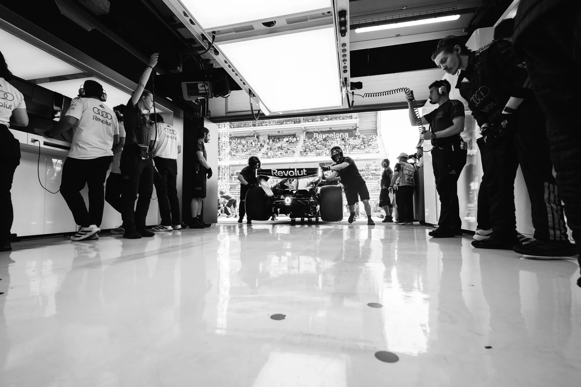 Black and white front view of an Audi Revolut F1® Team Formula One car being pushed into the garage by mechanics with crew members standing on both sides