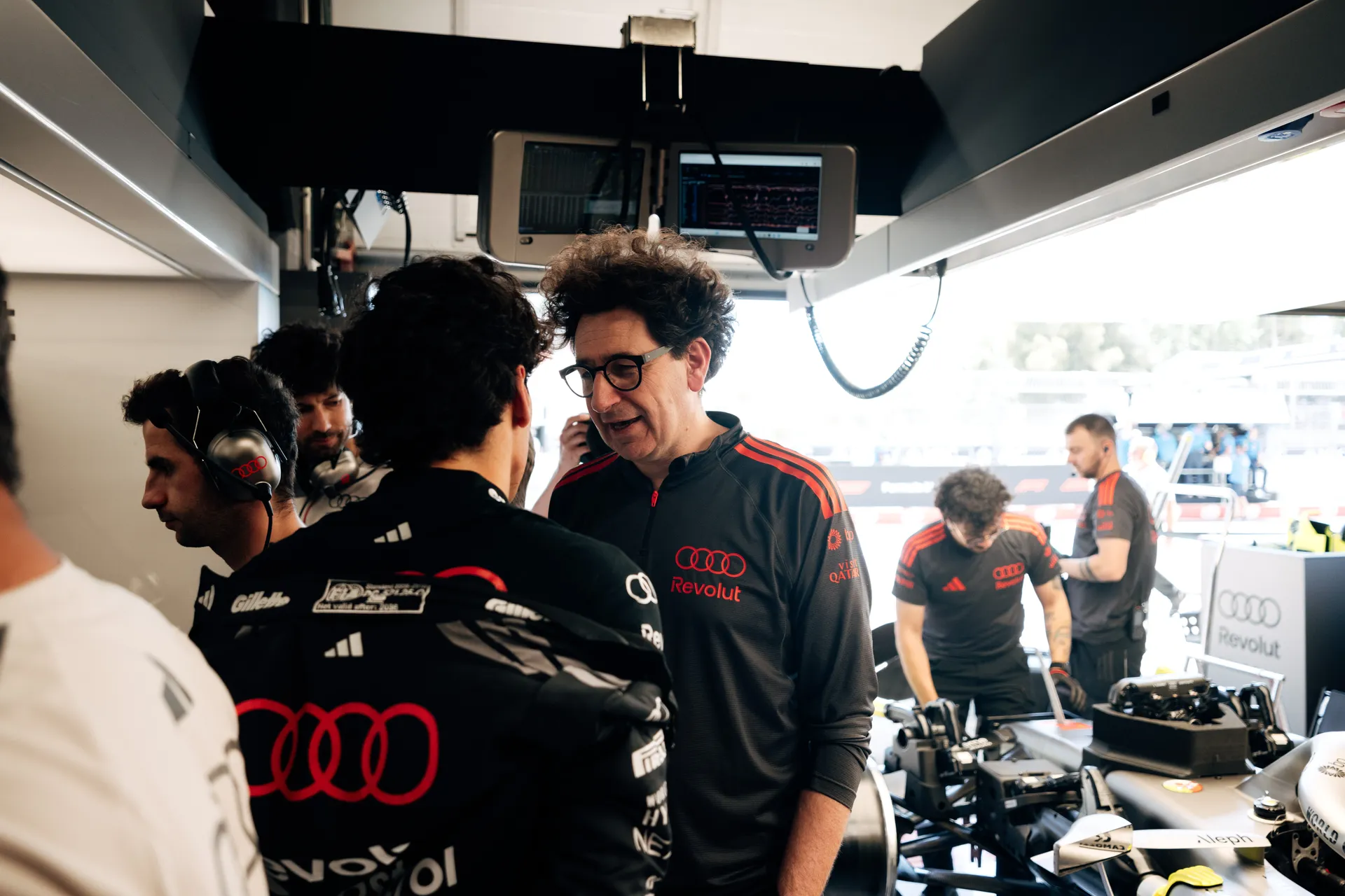 Audi Revolut F1® Team principal Mattia Binotto speaking with a driver inside the garage while engineers work on the car behind them in Barcelona