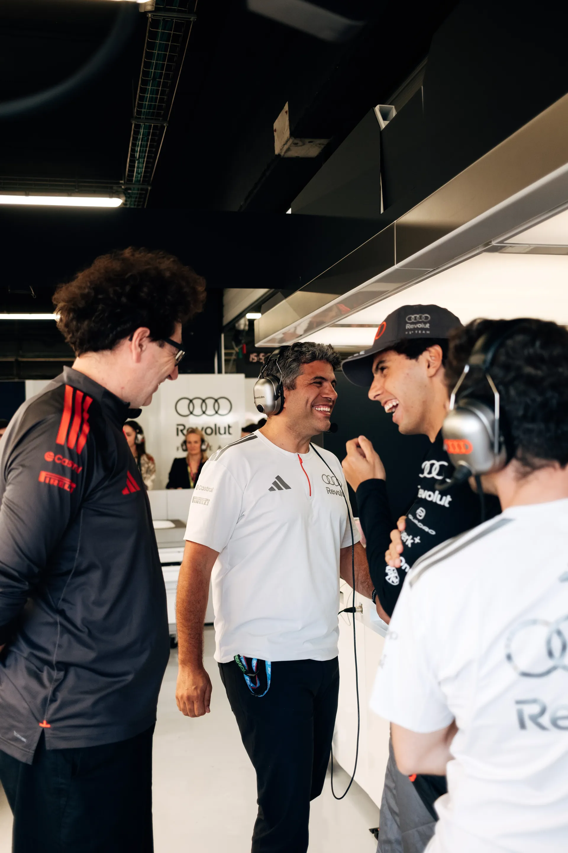 Gabriel Bortoleto smiling and talking with Mattia Binotto and Audi Revolut F1® Team engineers inside the garage during a light moment between sessions in Barcelona