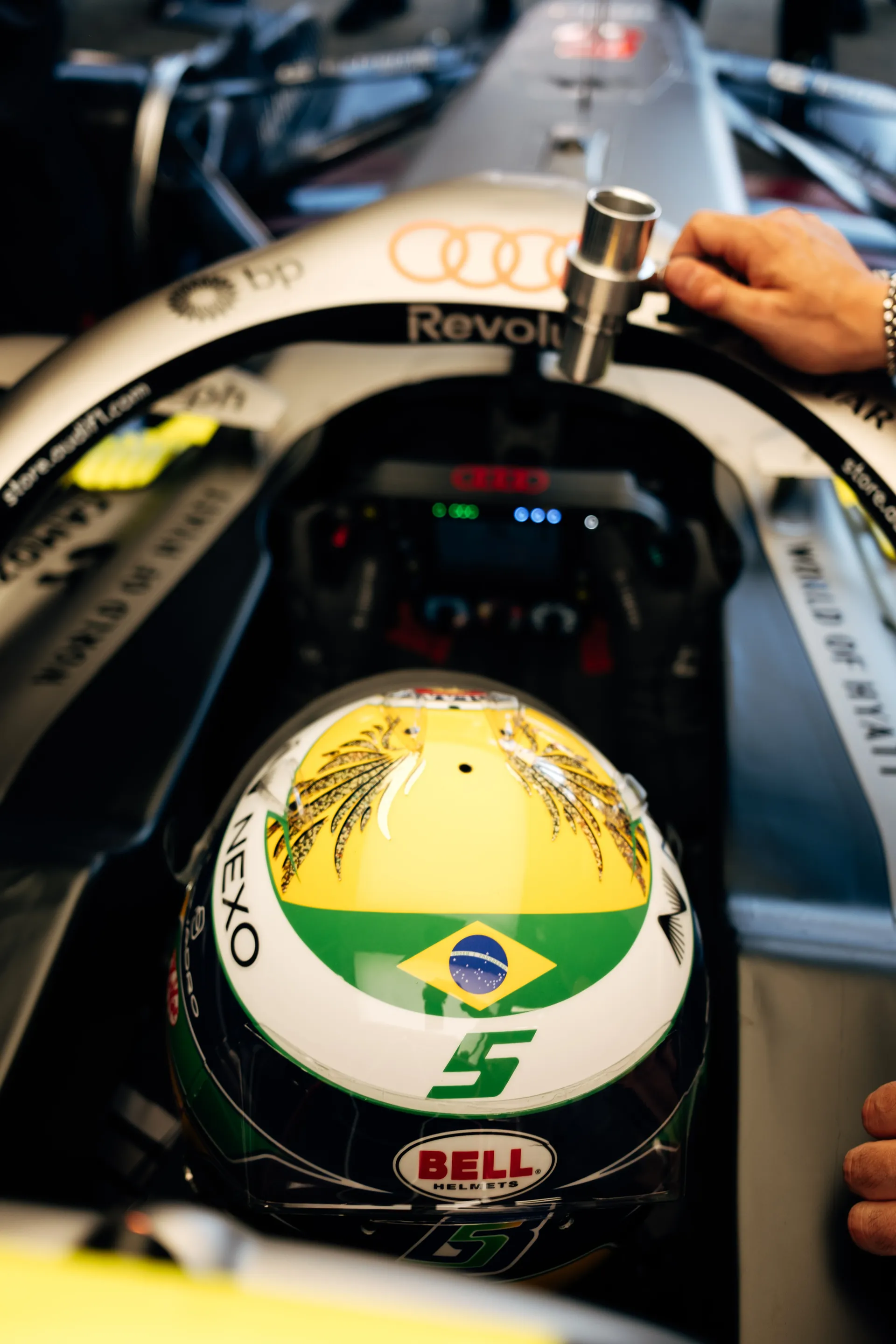 Close-up of Gabriel Bortoleto’s helmet with Brazilian flag and number 5 inside the Audi Revolut F1® Team cockpit while a mechanic works on the halo structure
