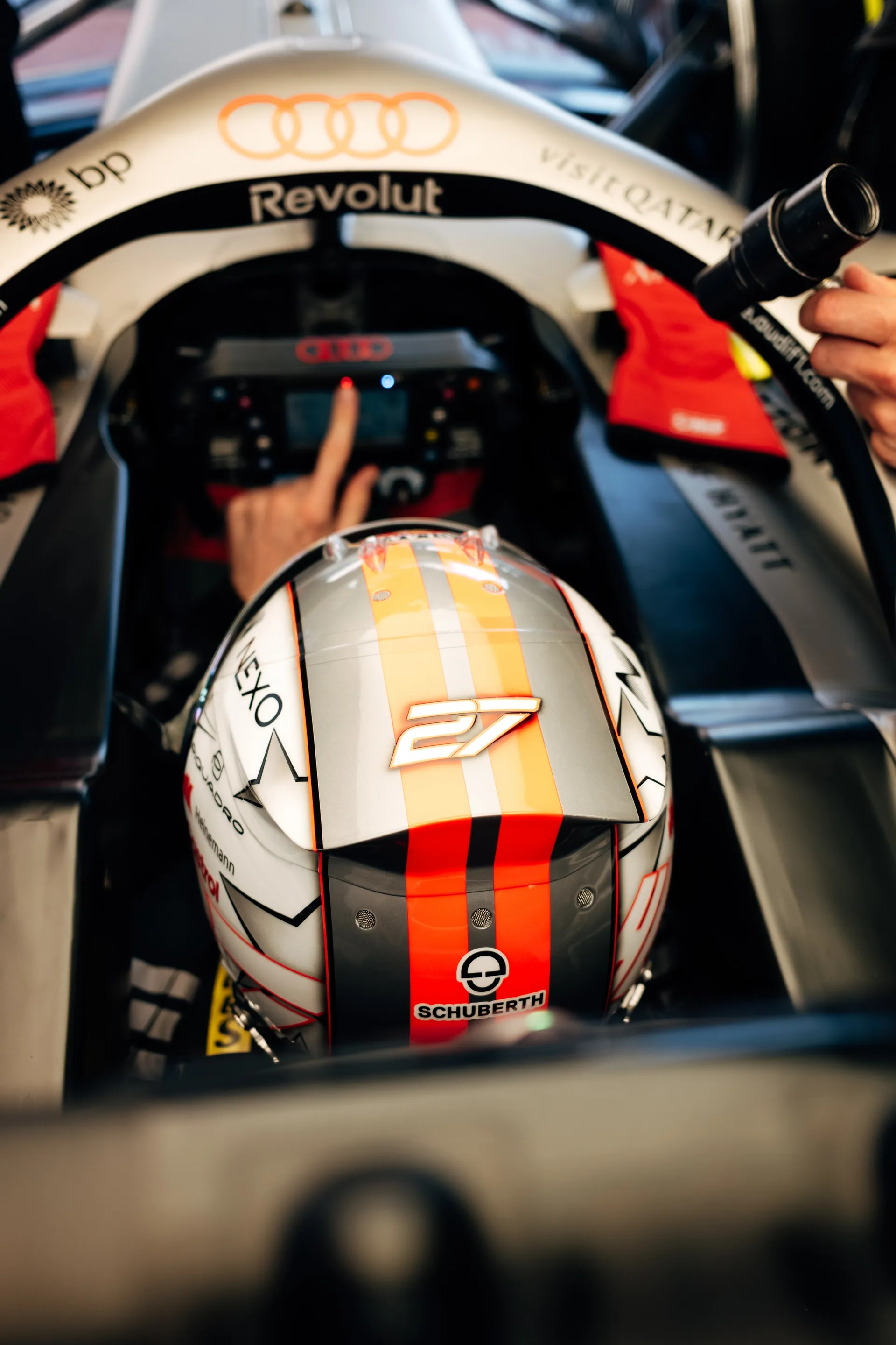 Top view of Nico Hulkenberg seated in the Audi Revolut F1® Team car with number 27 helmet, adjusting cockpit controls while a mechanic holds a cooling device